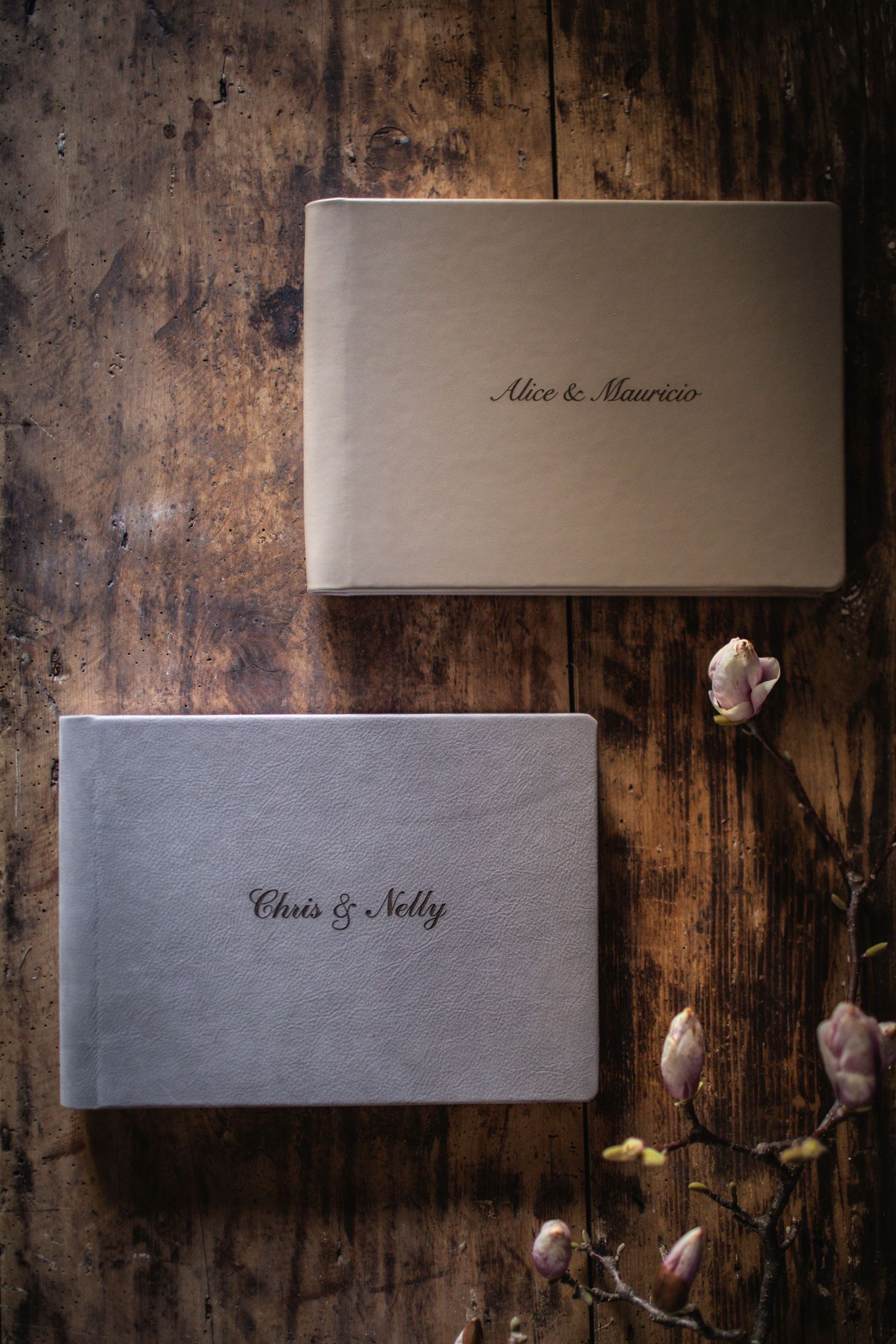 Two elegant personalized wedding photo albums on a rustic wooden surface with pink flowers.