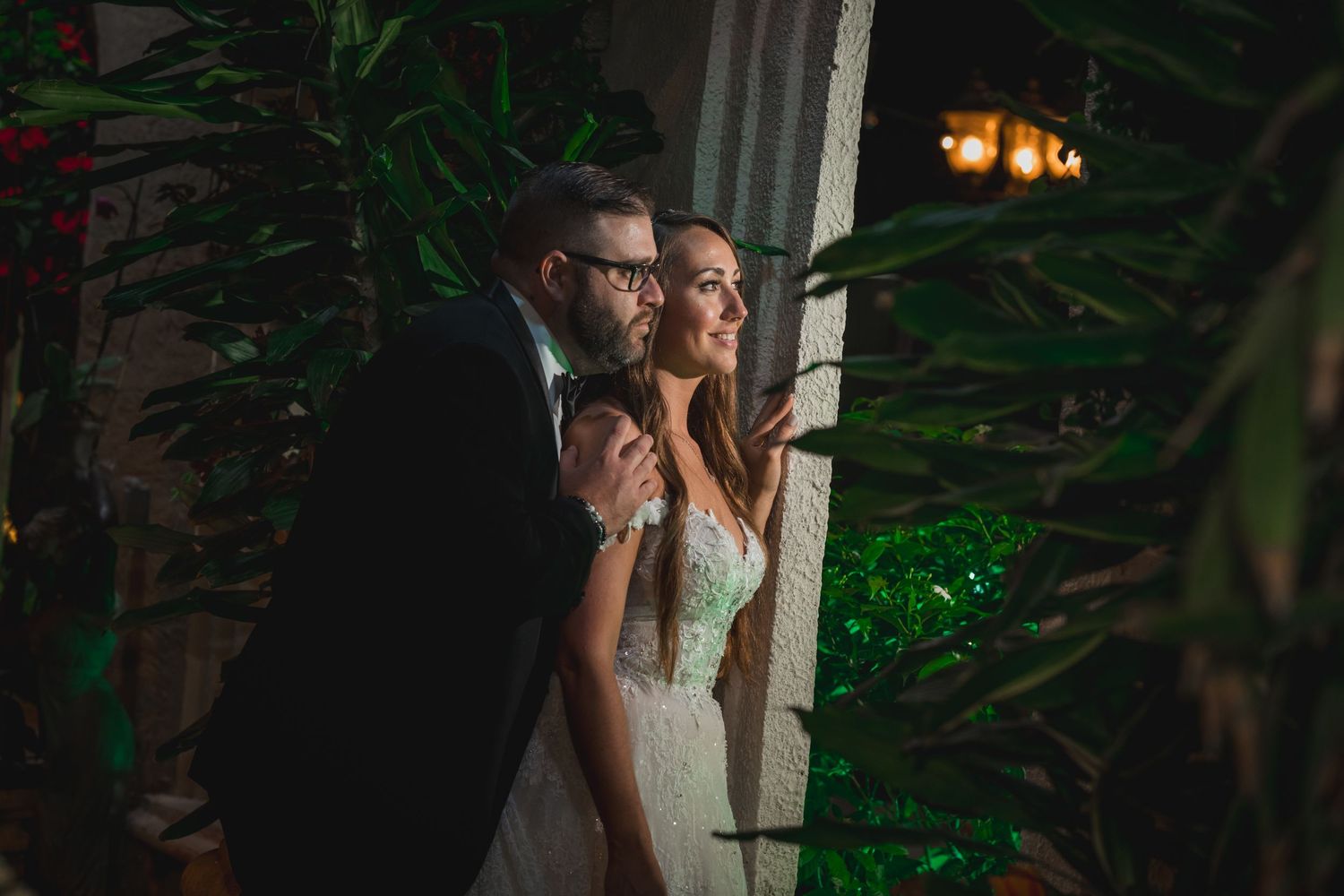 Bride and groom sharing romantic moment surrounded by lush greenery at night wedding.