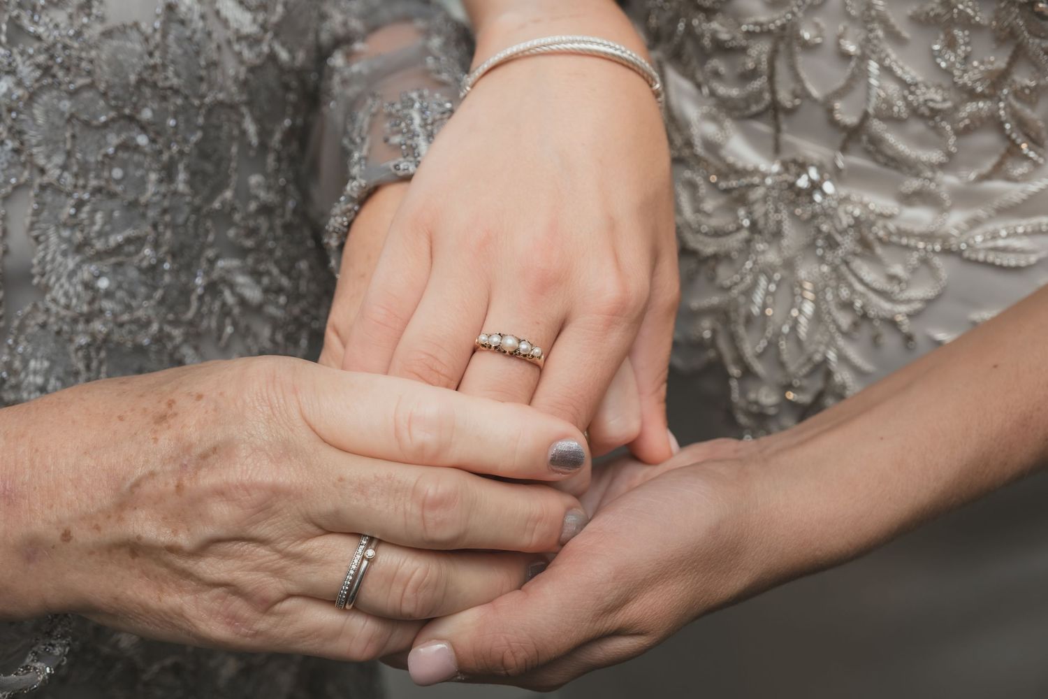 Close-up of bride and elder hands holding showing diamond engagement ring and bracelet.