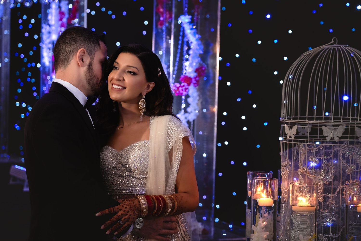 Indian bride and groom share romantic moment under sparkling blue bokeh lights.