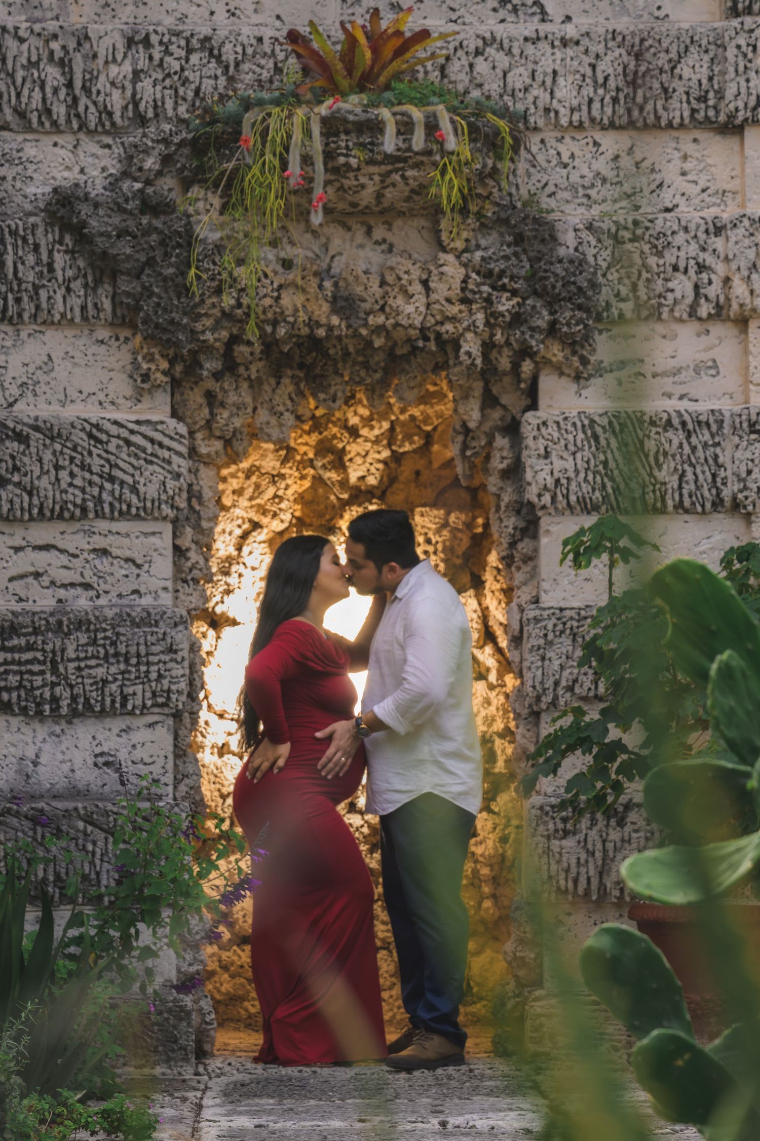 Couple sharing a kiss in a glowing stone archway surrounded by lush tropical greenery.
