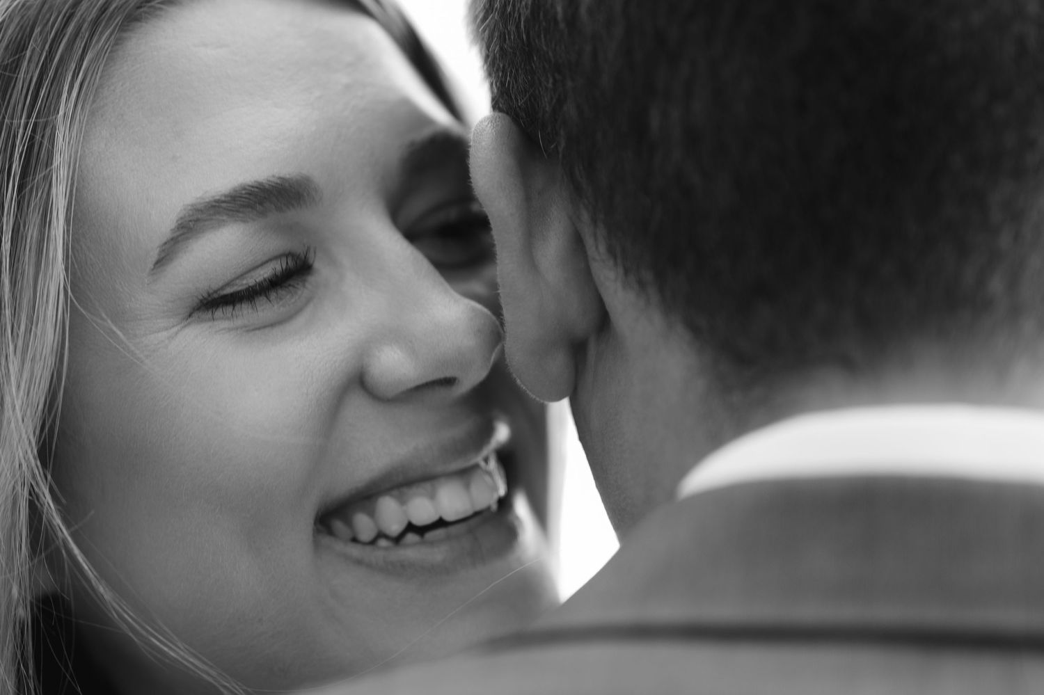 Joyful bride smiling closely at groom in black and white portrait.