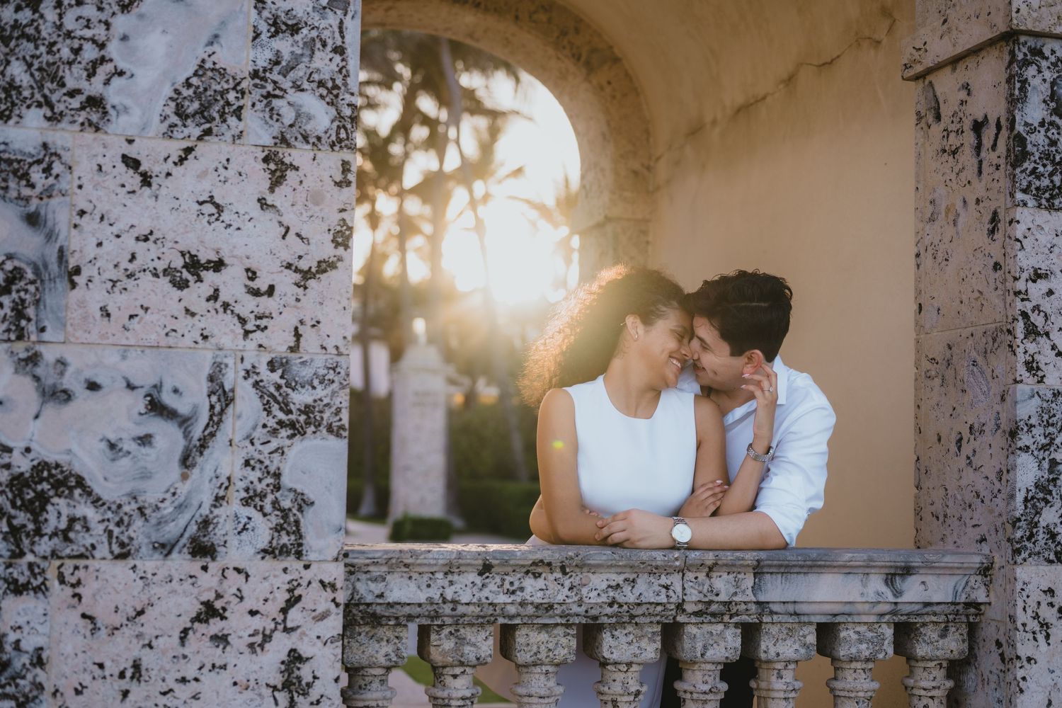 Romantic couple sharing intimate moment on stone balcony at golden sunset.