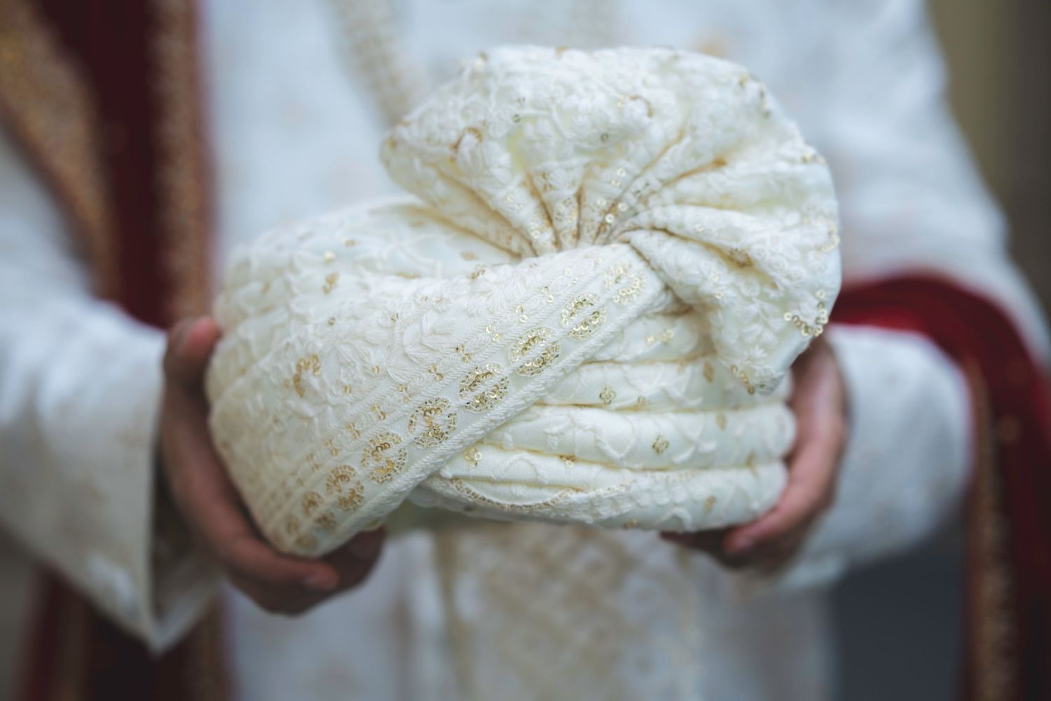 Close-up of groom holding an ornate cream and gold embroidered turban pagri for Indian wedding ceremony.