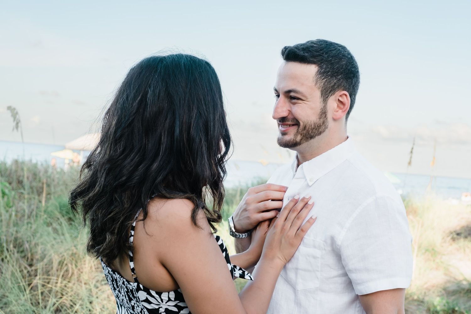 Smiling man in white shirt gazing at dark-haired woman during outdoor engagement photo session.