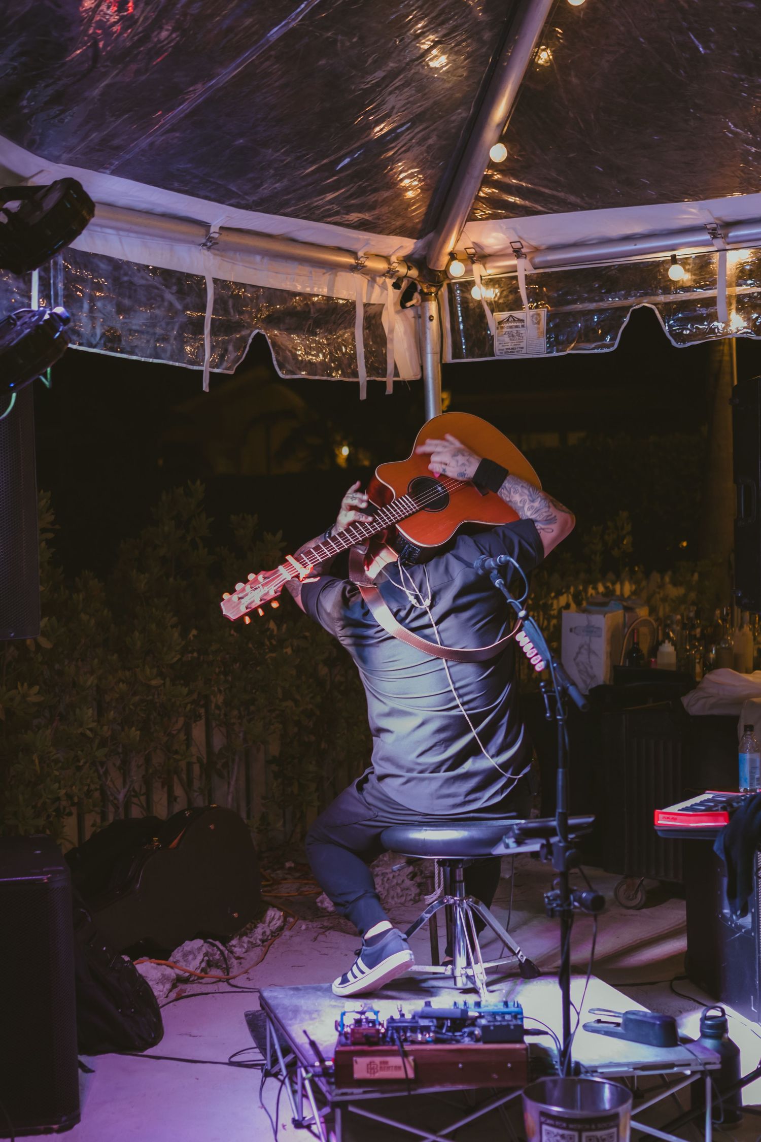 Bearded guitarist in orange hat performs passionately on stage under purple lights at wedding.