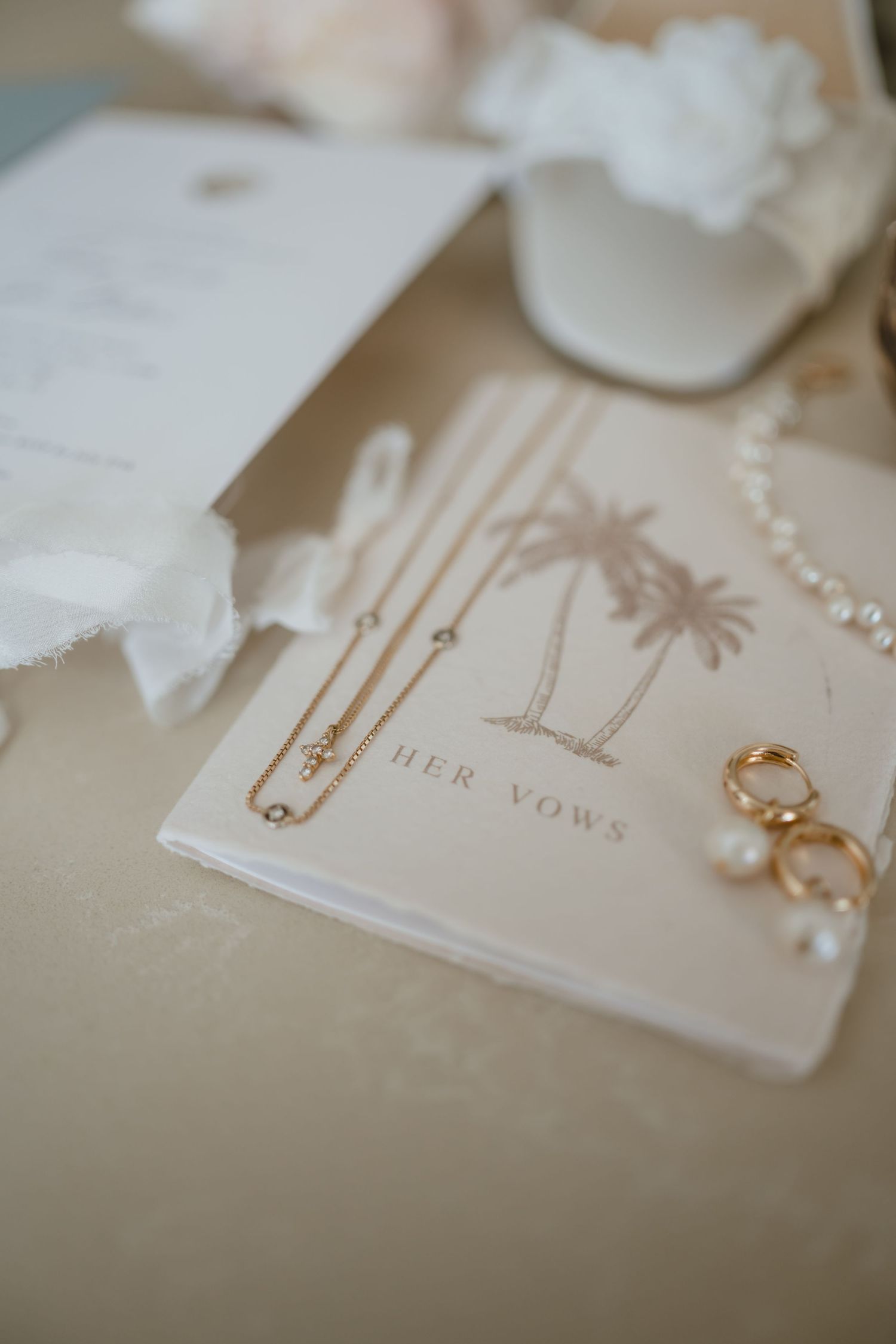 Wedding flat lay with vow book, gold necklace, rings, pearls, and bridal accessories.