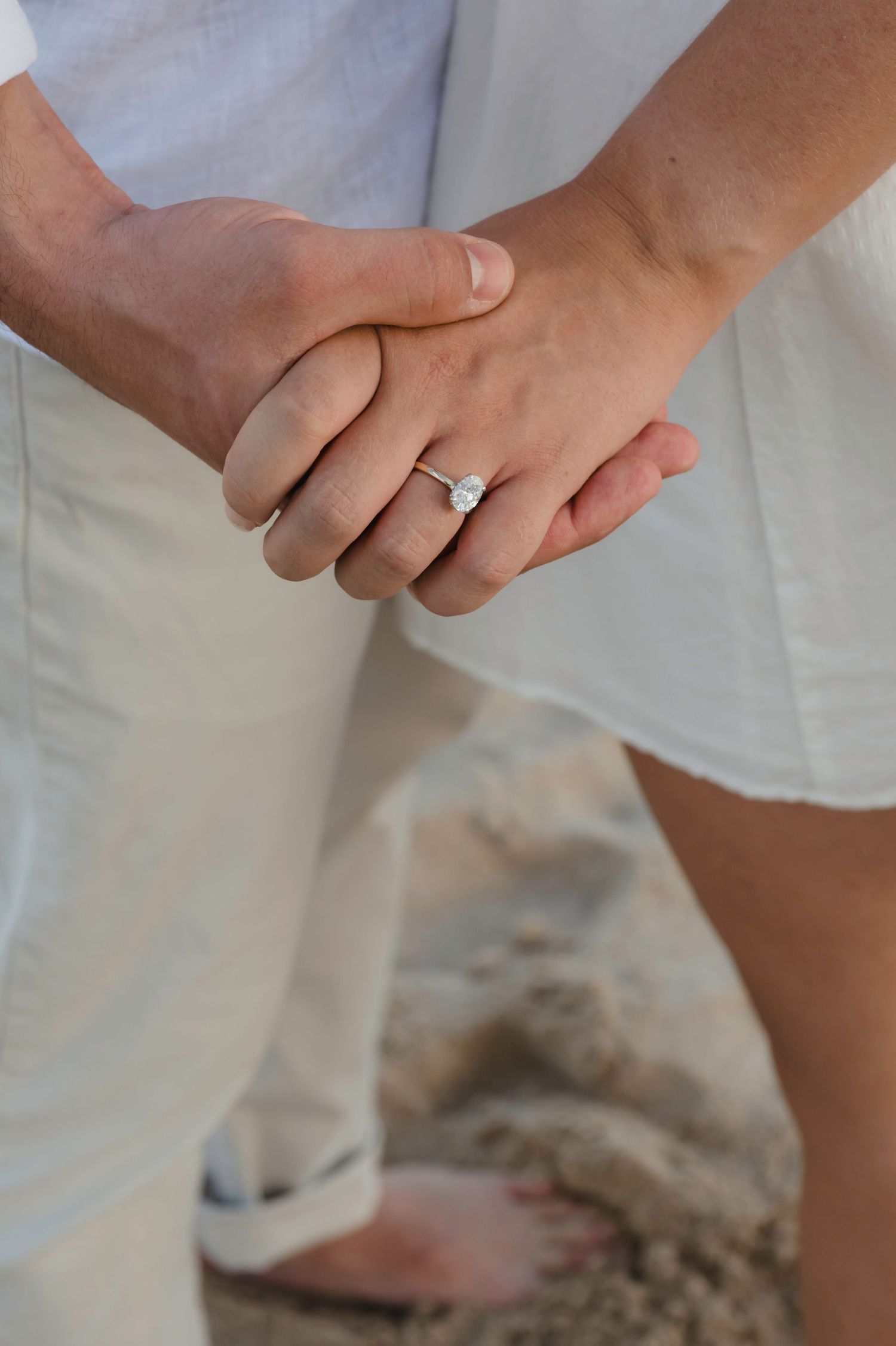 Close-up of a couple holding hands on the beach showcasing a beautiful diamond engagement ring.