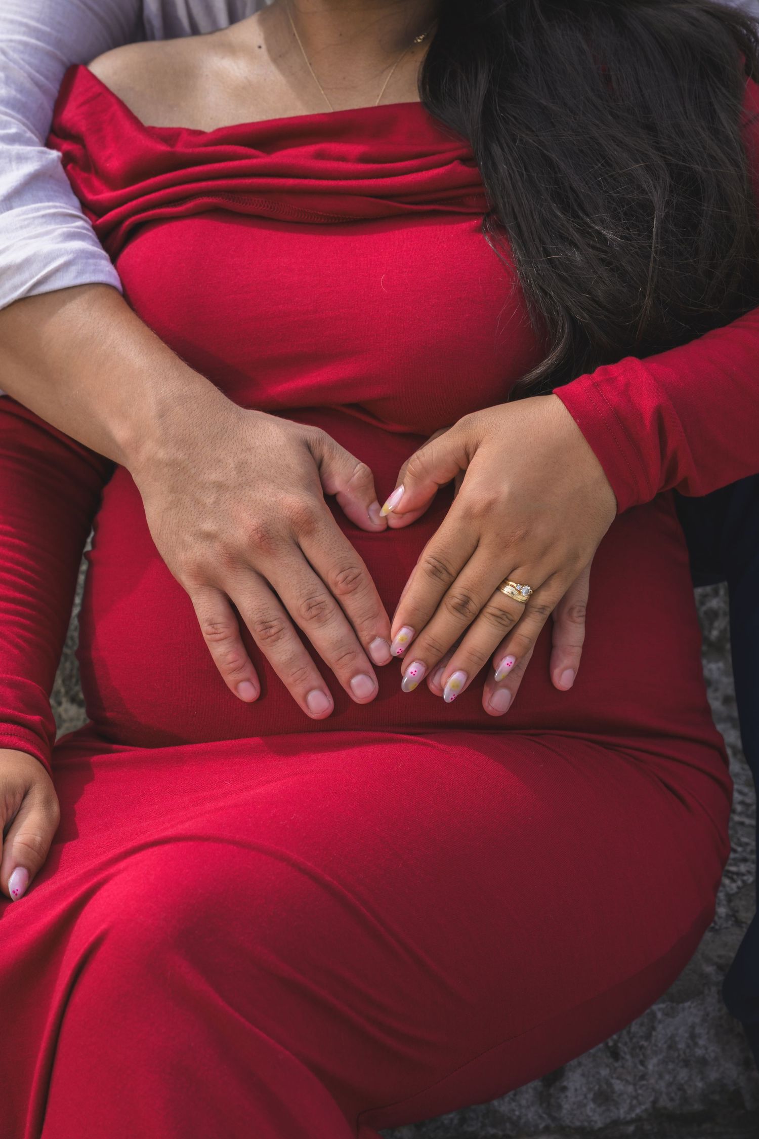 Couple forming heart shape with hands on pregnant belly in red maternity dress.