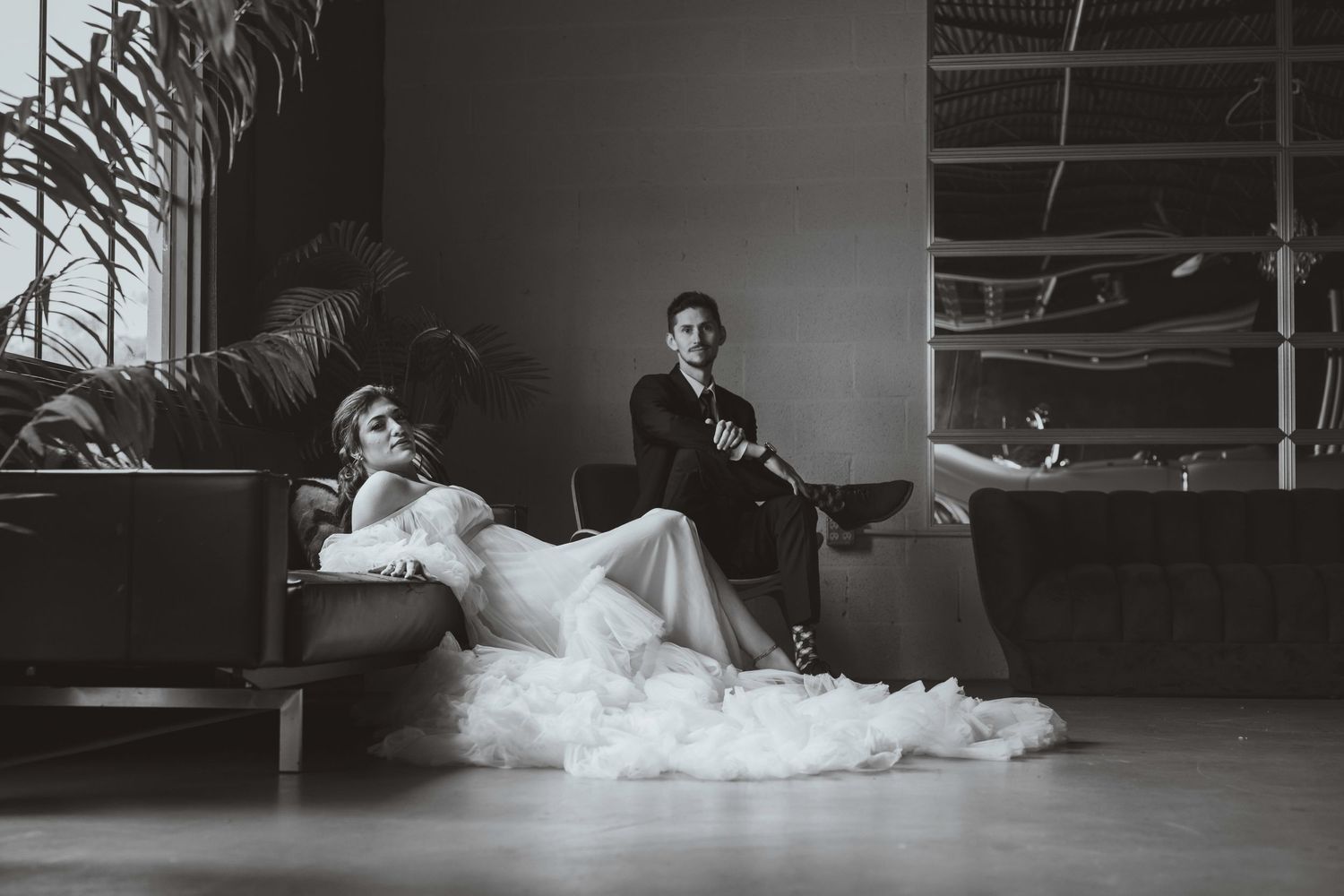 Elegant black and white wedding portrait of bride in ruffled gown and groom on modern sofa.