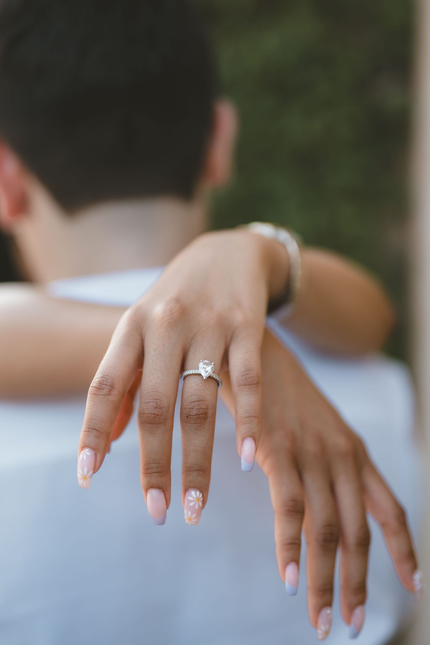 Close-up of a womans hands showing a heart-shaped diamond engagement ring with pink manicured nails.