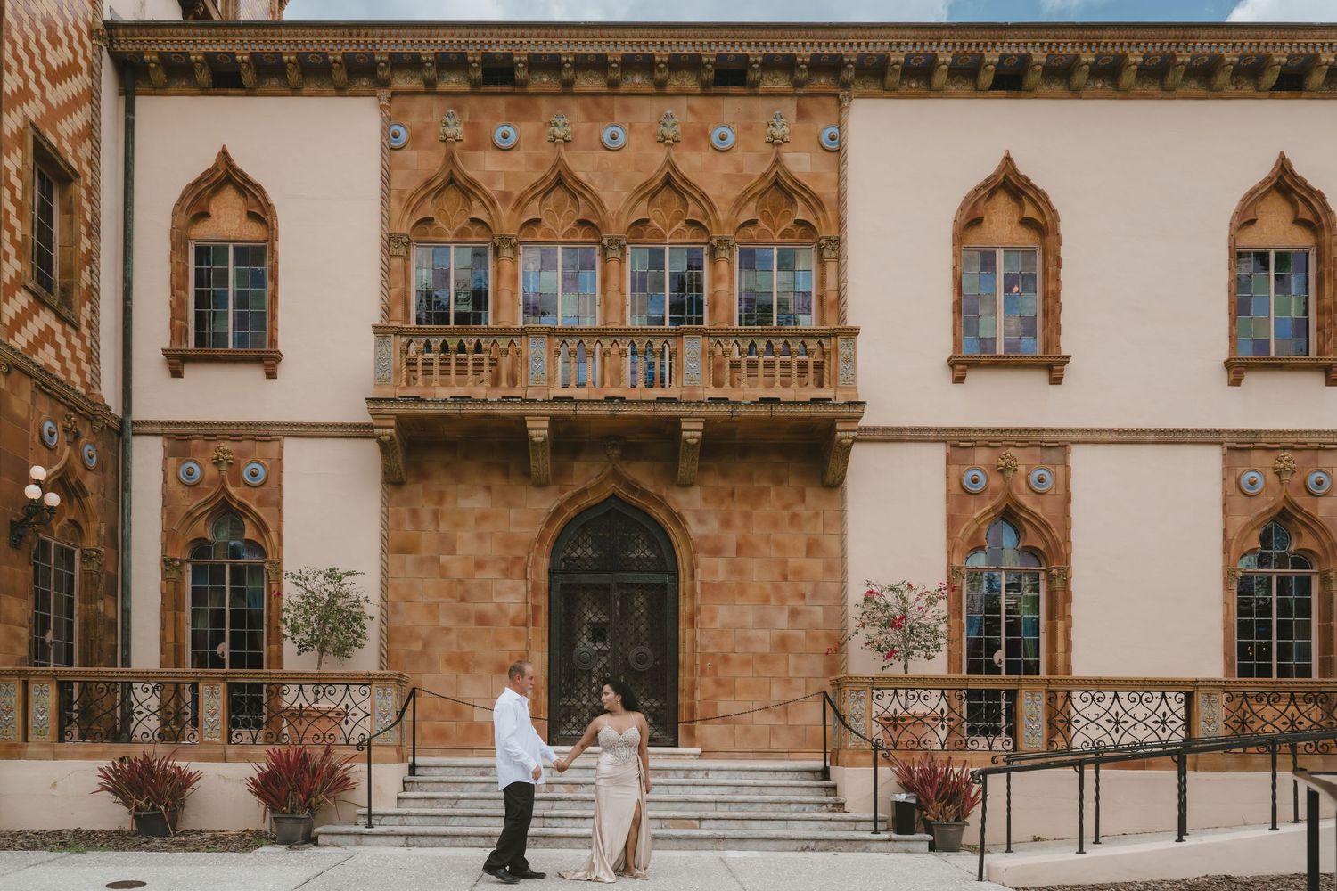 Couple posing in front of an ornate Gothic-style building with arched windows and decorative stonework.