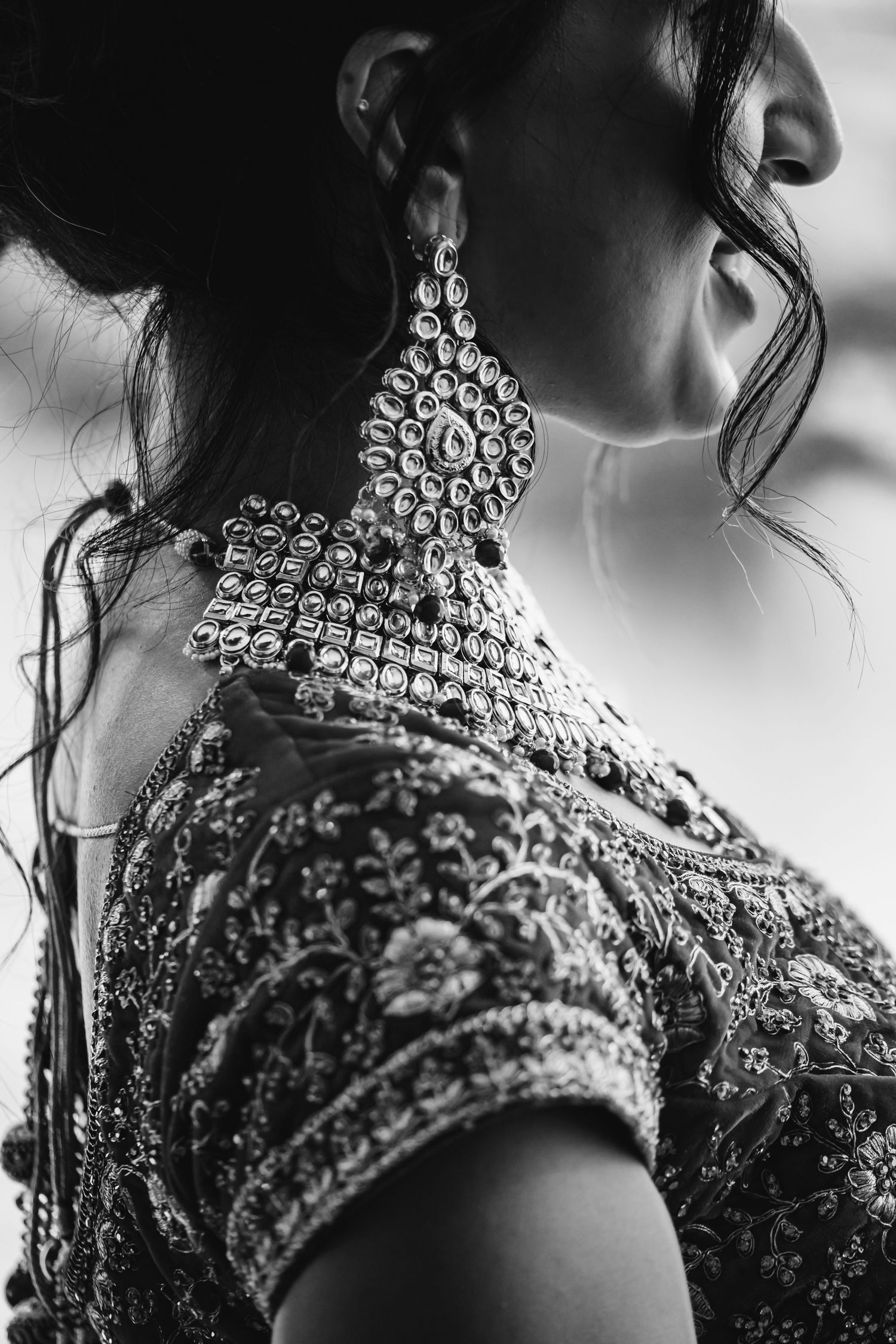 Black and white close-up of Indian bride wearing ornate chandelier earring and embroidered lehenga.