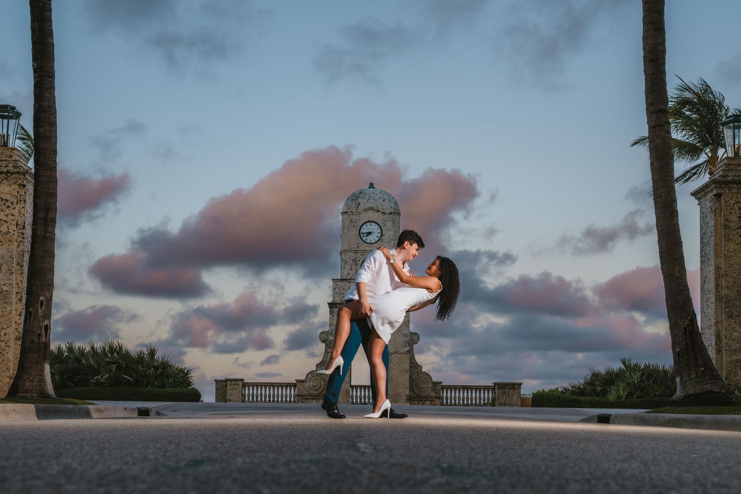 Romantic couple sharing a dip kiss with clock tower backdrop at dusk.
