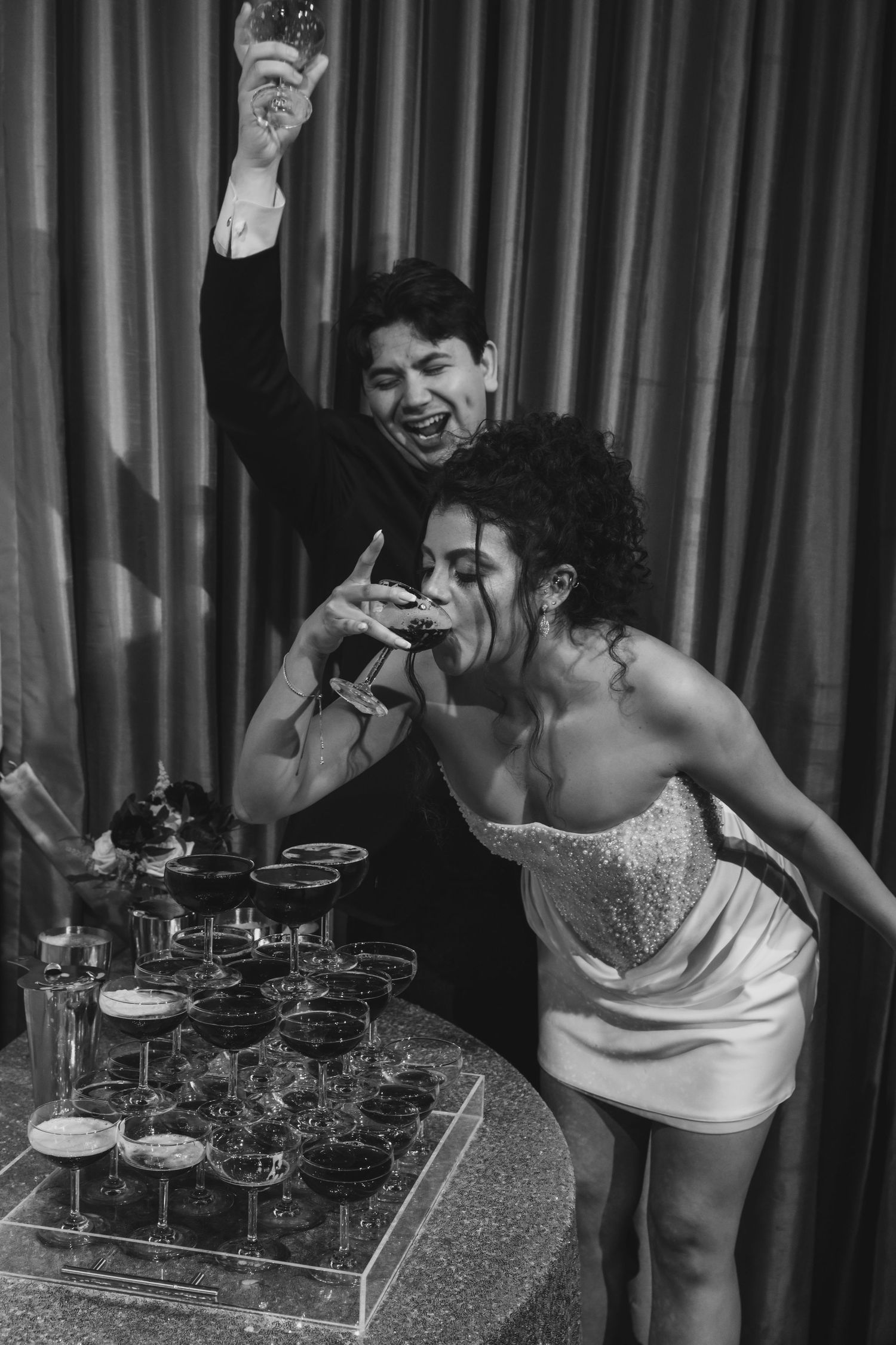 Black and white photo of excited bride and groom celebrating at champagne tower wedding reception.
