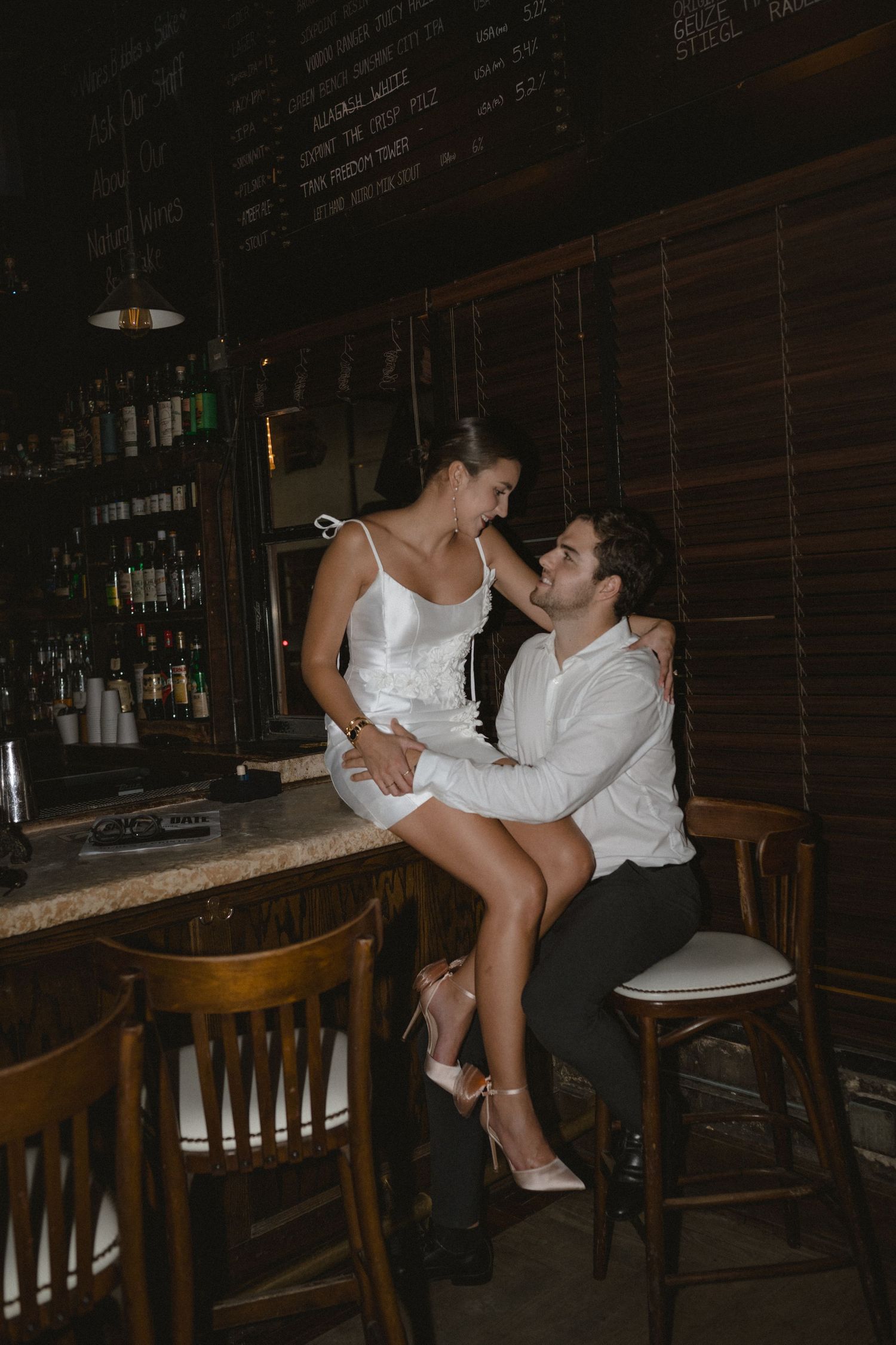 Couple sharing an intimate moment at a dimly lit bar, with the woman seated on the counter.