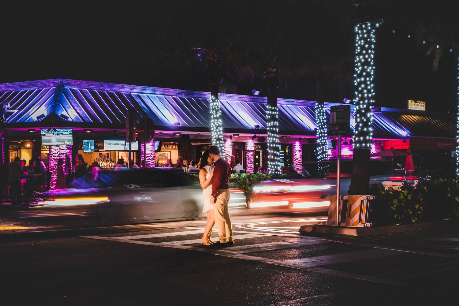 Couple embracing on a city street at night surrounded by vibrant neon lights and light trails.