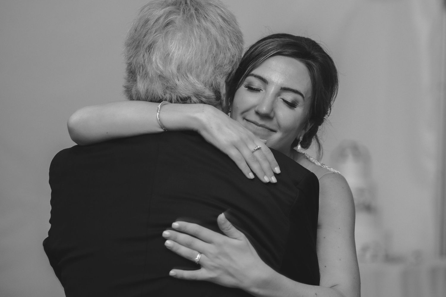 Emotional black and white photo of a bride hugging an elderly guest at a wedding.