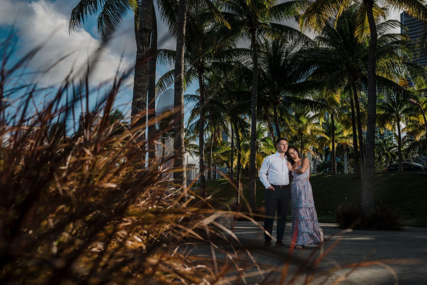 Couple embracing among tall palm trees in a tropical outdoor setting at golden hour.