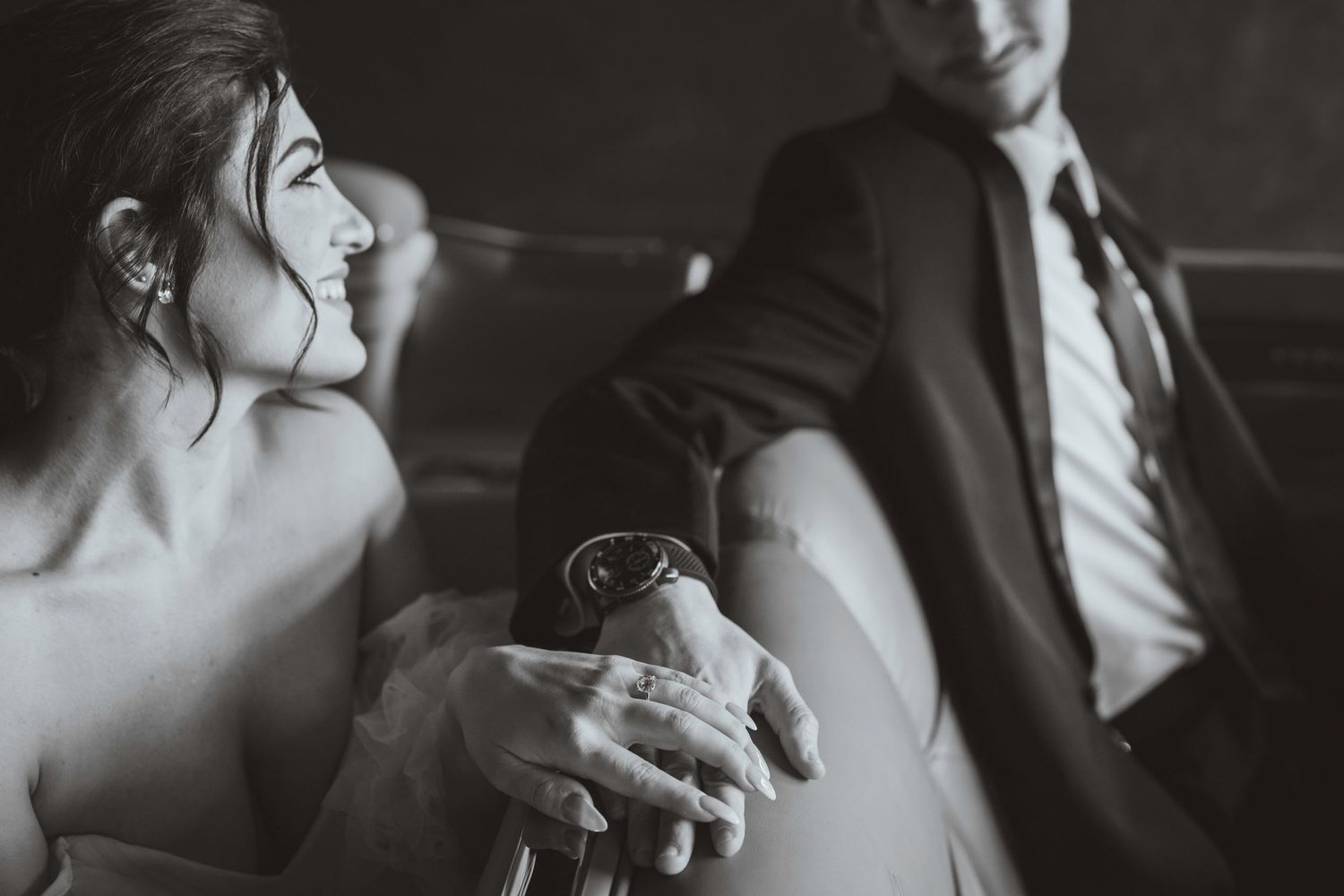Black and white photo of bride smiling at groom while holding a wine bottle at their wedding reception.