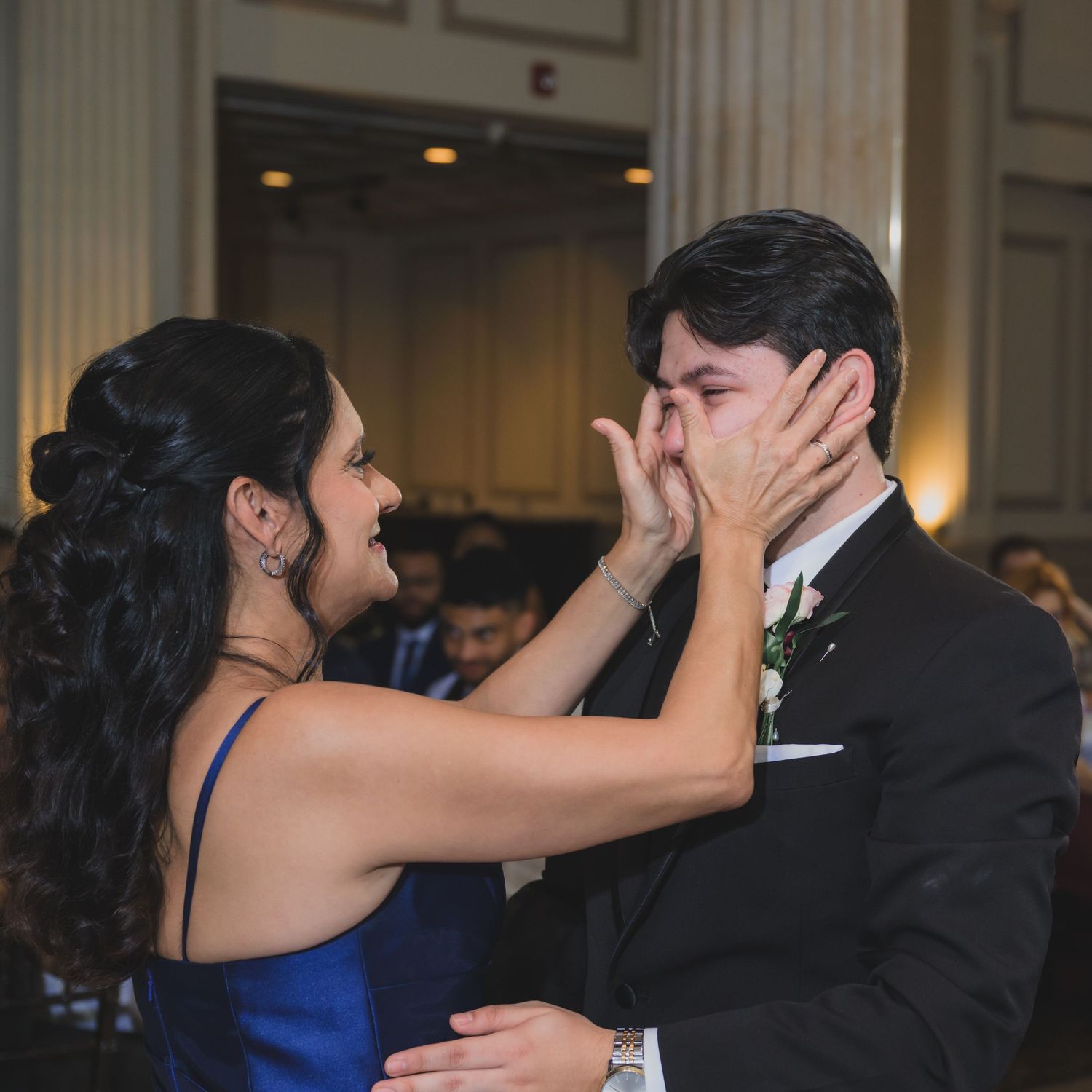 A woman in a blue dress tenderly cups a man's face in a formal ballroom setting during a wedding reception.