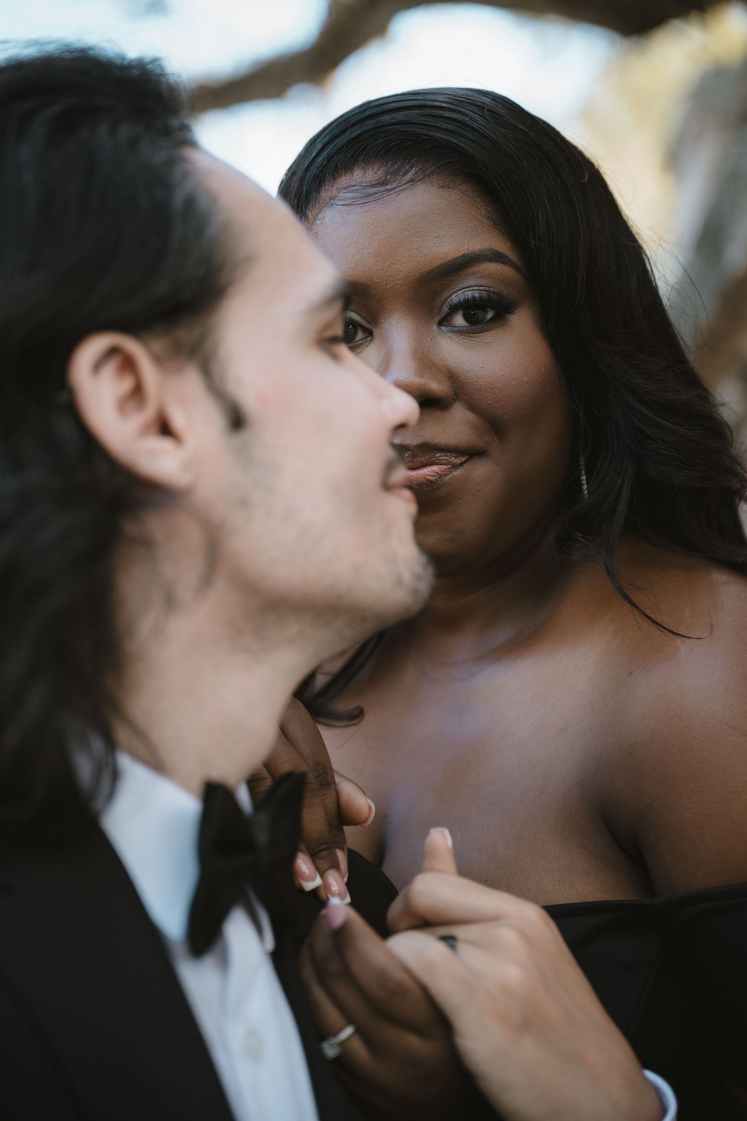 Interracial couple sharing a tender kiss during a romantic outdoor engagement portrait session.