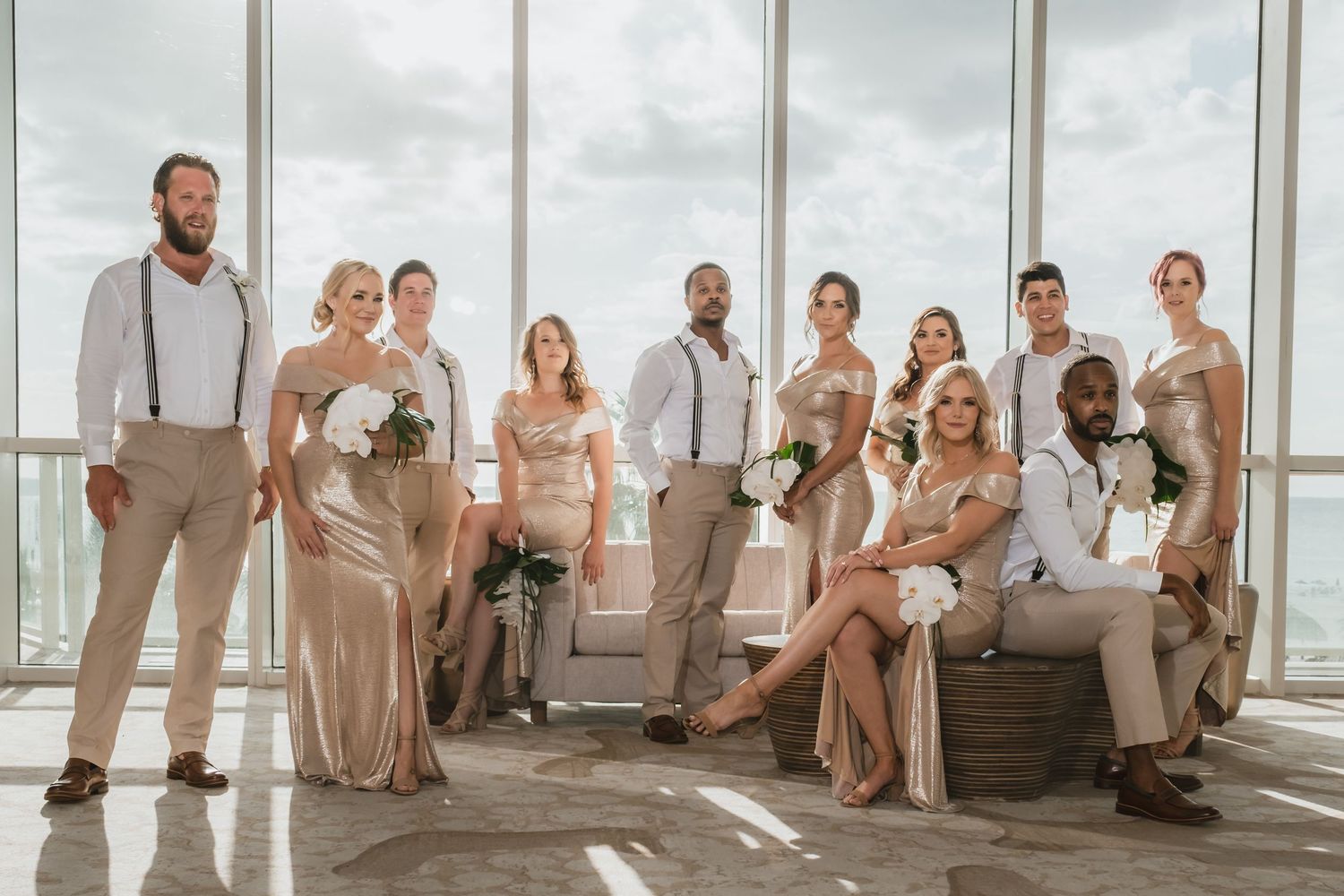 Wedding party in gold and white attire posing together in a sunlit modern venue.