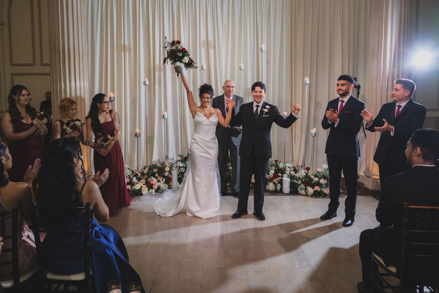 Bride and groom celebrate at wedding ceremony altar surrounded by cheering guests in elegant ballroom venue.