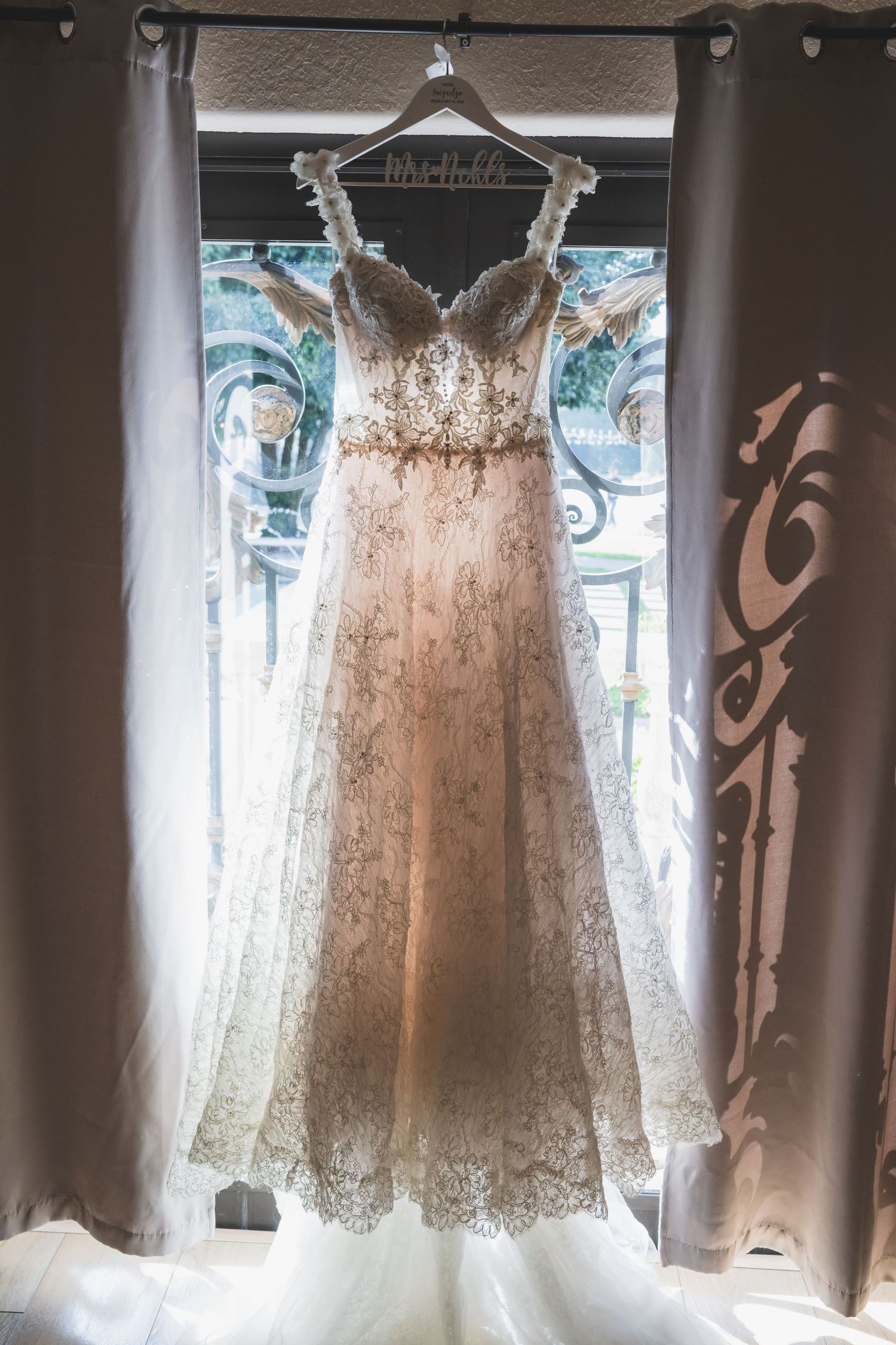 Elegant lace A-line wedding dress with beaded belt hanging in a window with ornate iron details.