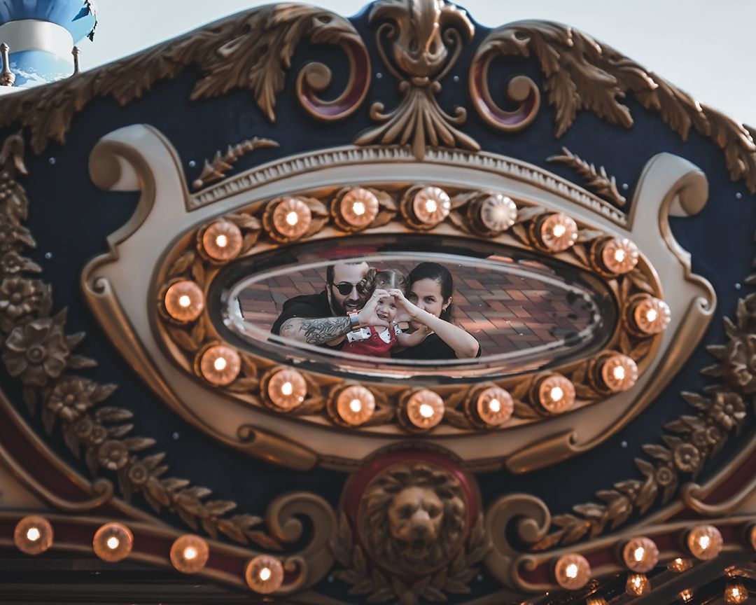 Couple reflected in ornate carousel mirror surrounded by vintage lights and gold decor.