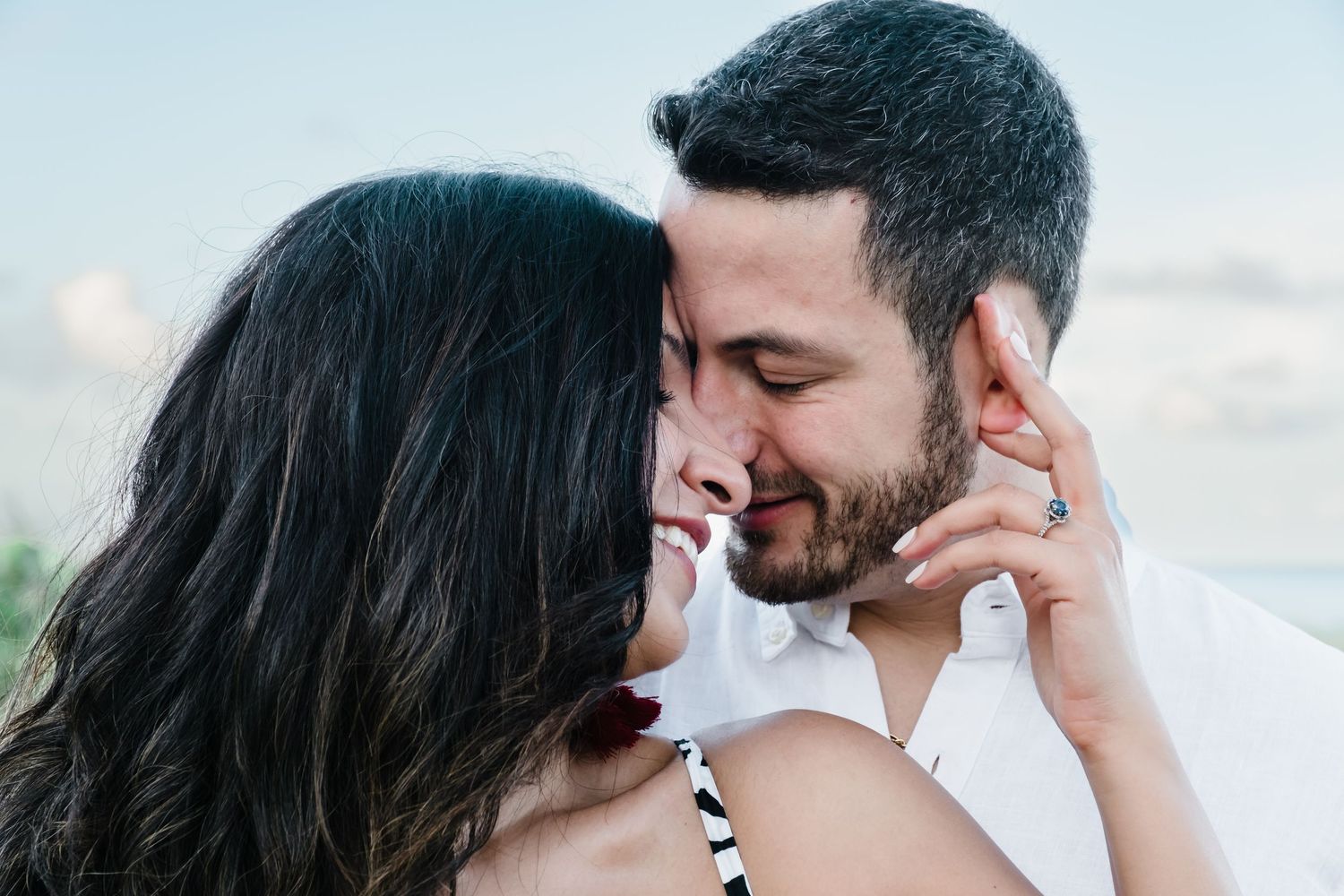 Happy couple sharing an intimate moment, woman wearing engagement ring embracing man outdoors.