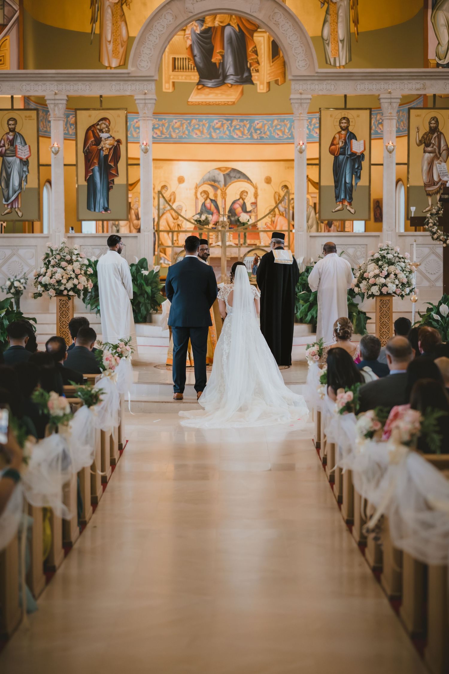 Bride and groom stand at ornate church altar during traditional wedding ceremony with guests seated.