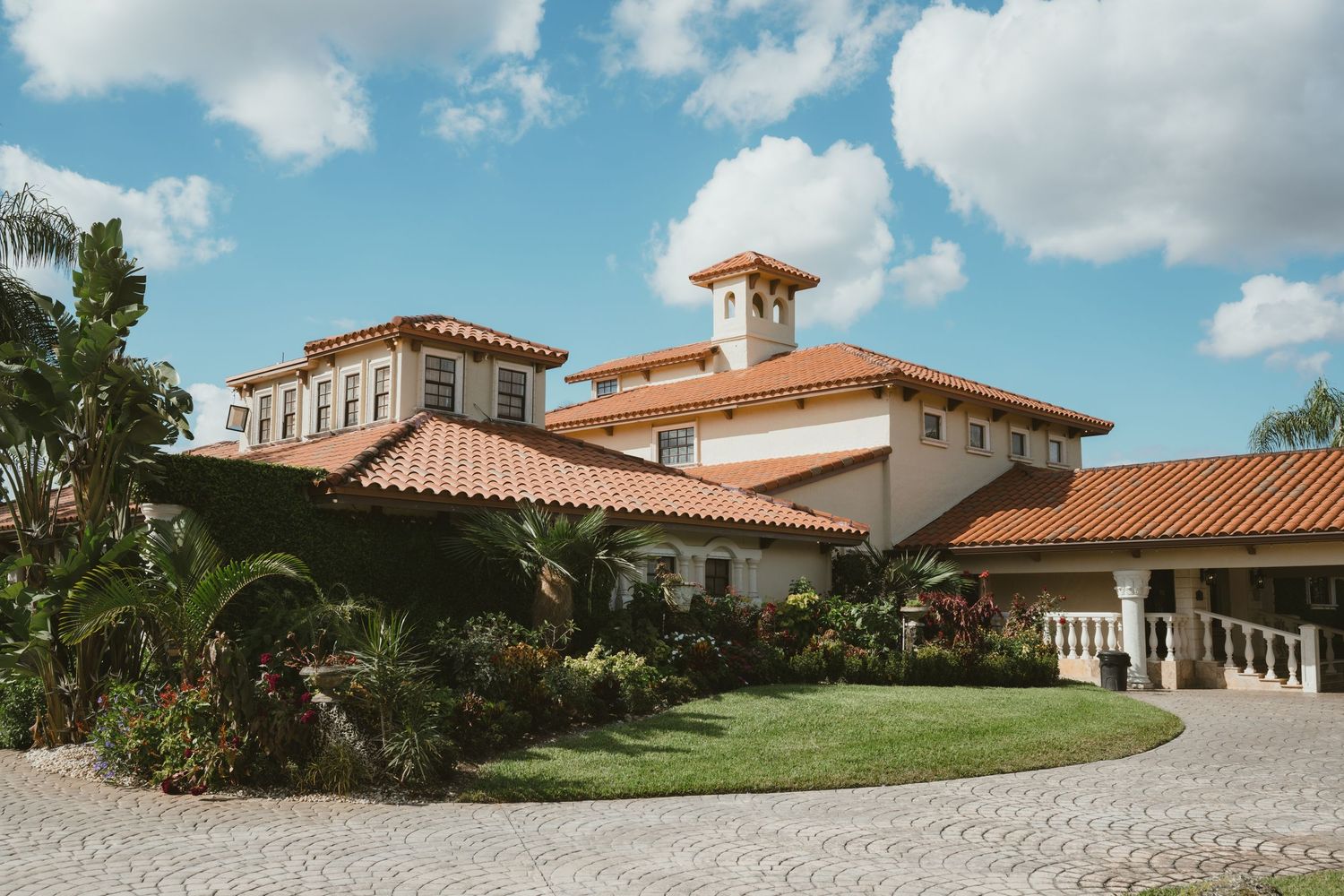 Spanish-style wedding venue with terracotta roof tiles and tropical landscaping under blue sky.