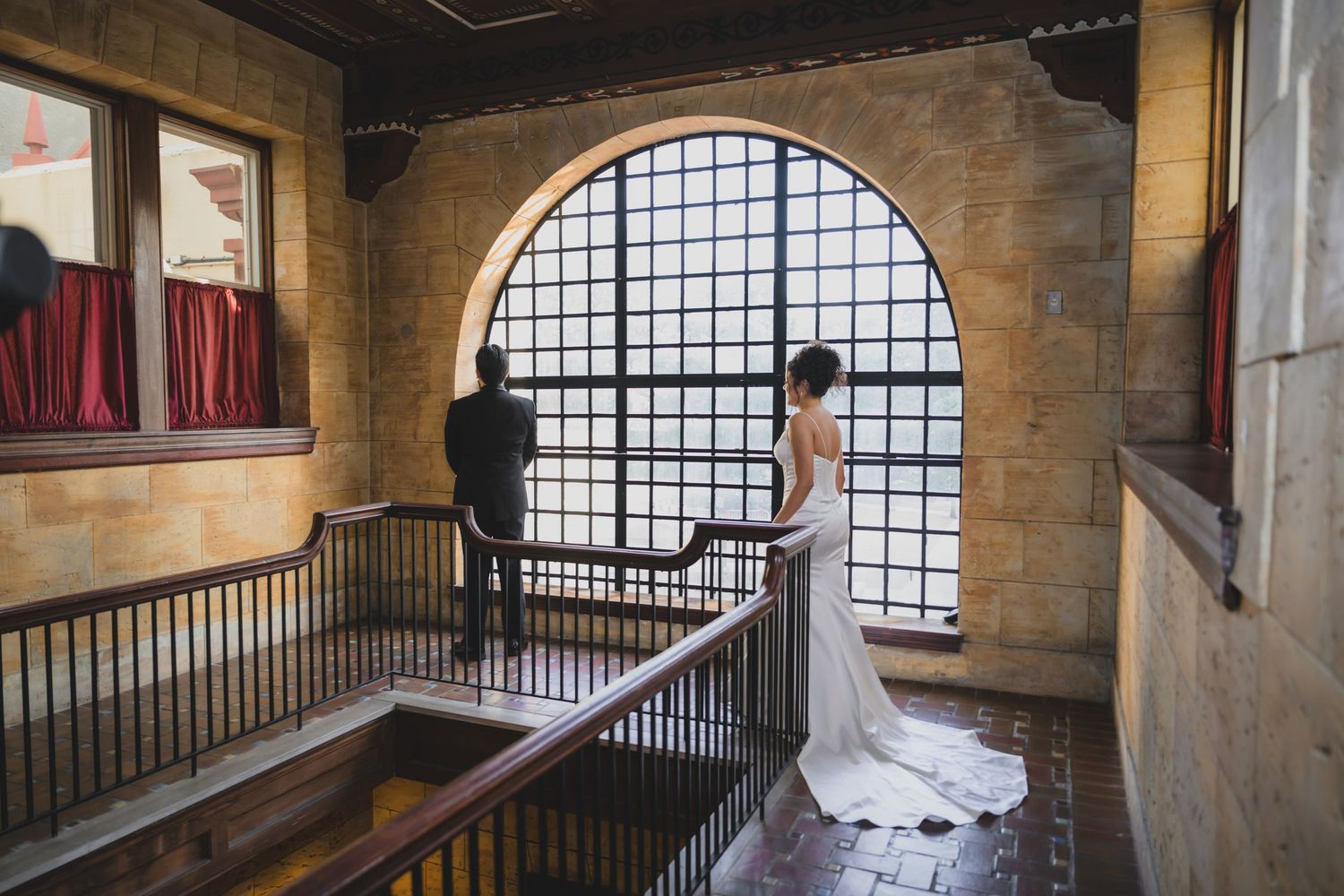 Bride and groom standing by an arched stone window in an elegant historic venue during their wedding ceremony.