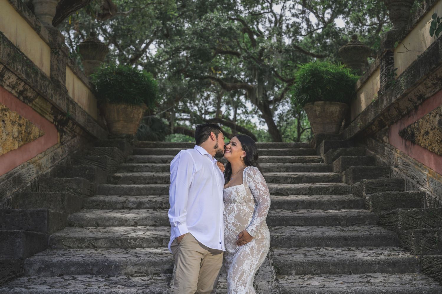 Couple sharing a romantic moment on stone steps surrounded by lush trees at Vizcaya Museum Gardens.