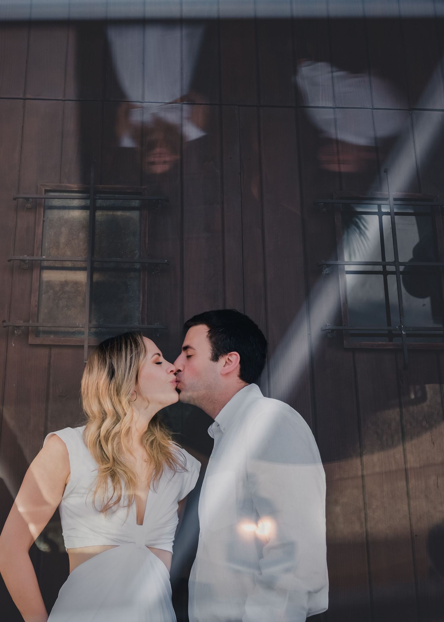 Couple sharing a kiss with artistic light reflections on glass backdrop.