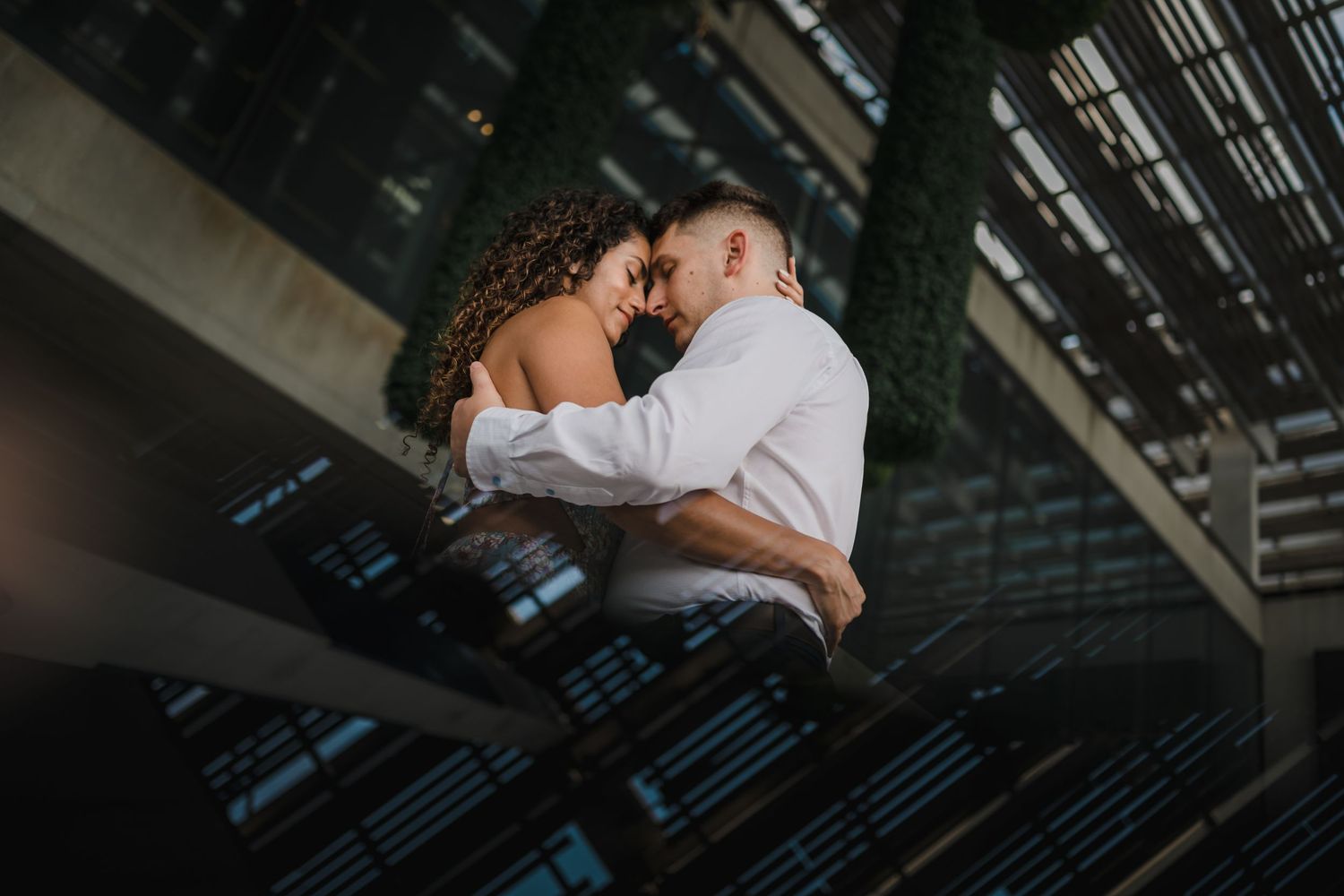 Couple sharing an intimate forehead touch while embracing on a modern architectural staircase.