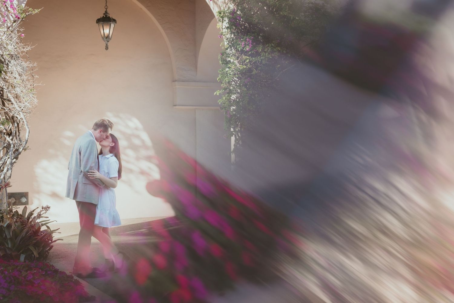 Couple embracing romantically under arched columns surrounded by vibrant blooming bougainvillea flowers.