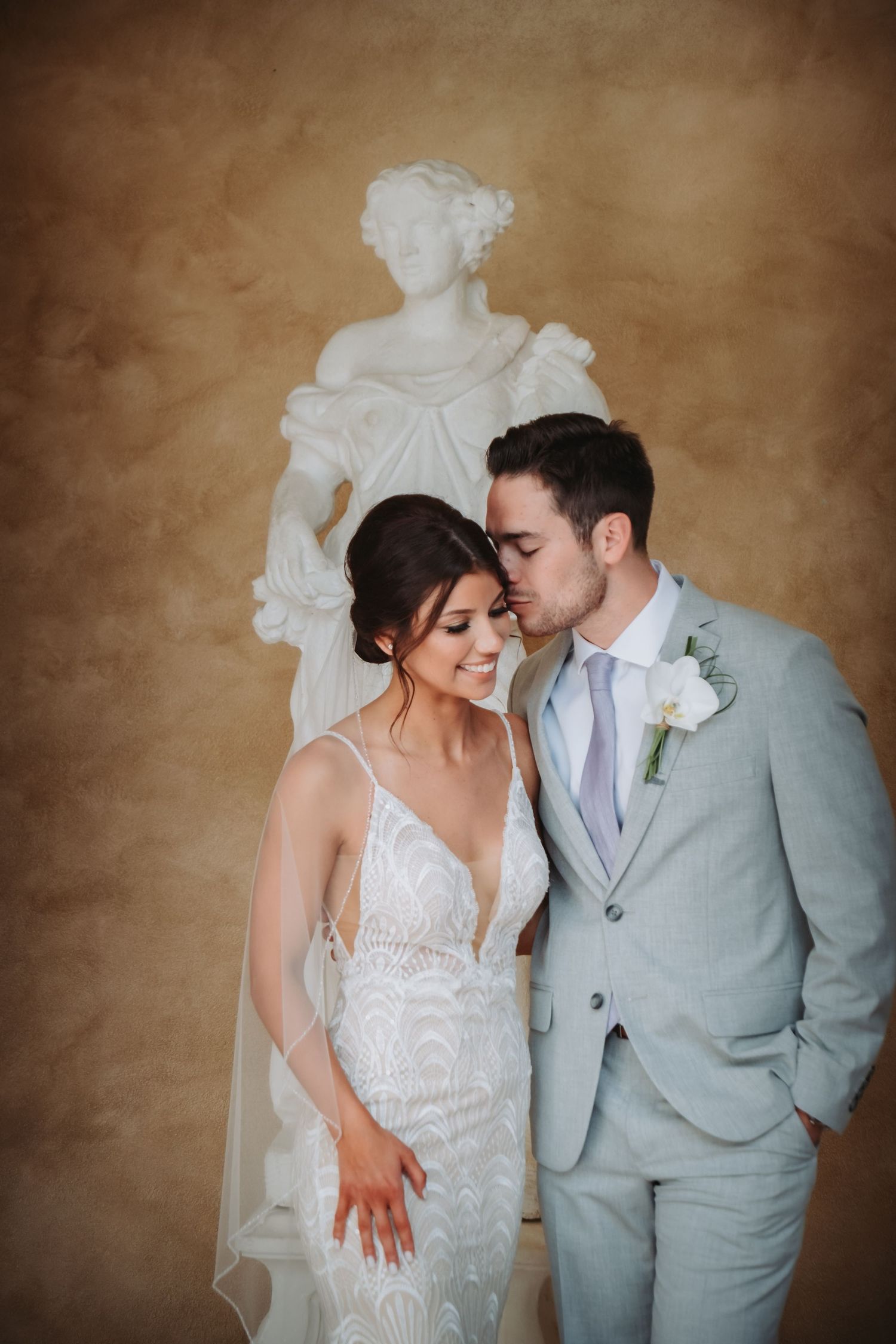 Bride and groom share a romantic moment in front of a classical white marble statue.