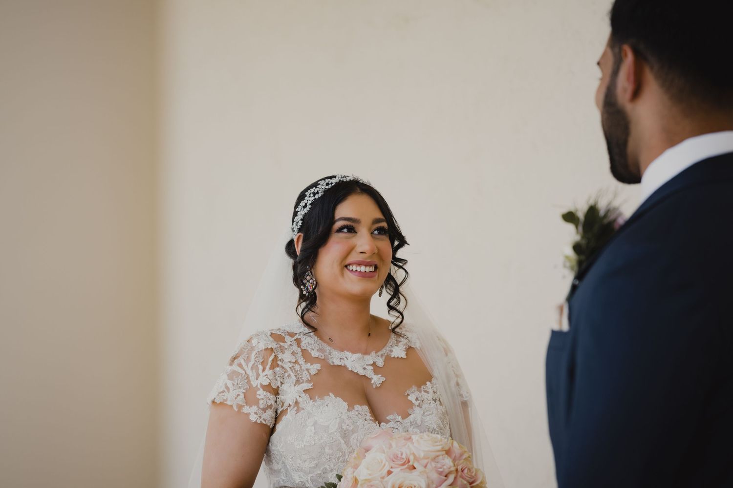 Bride in lace wedding gown smiling at groom during emotional first look moment.