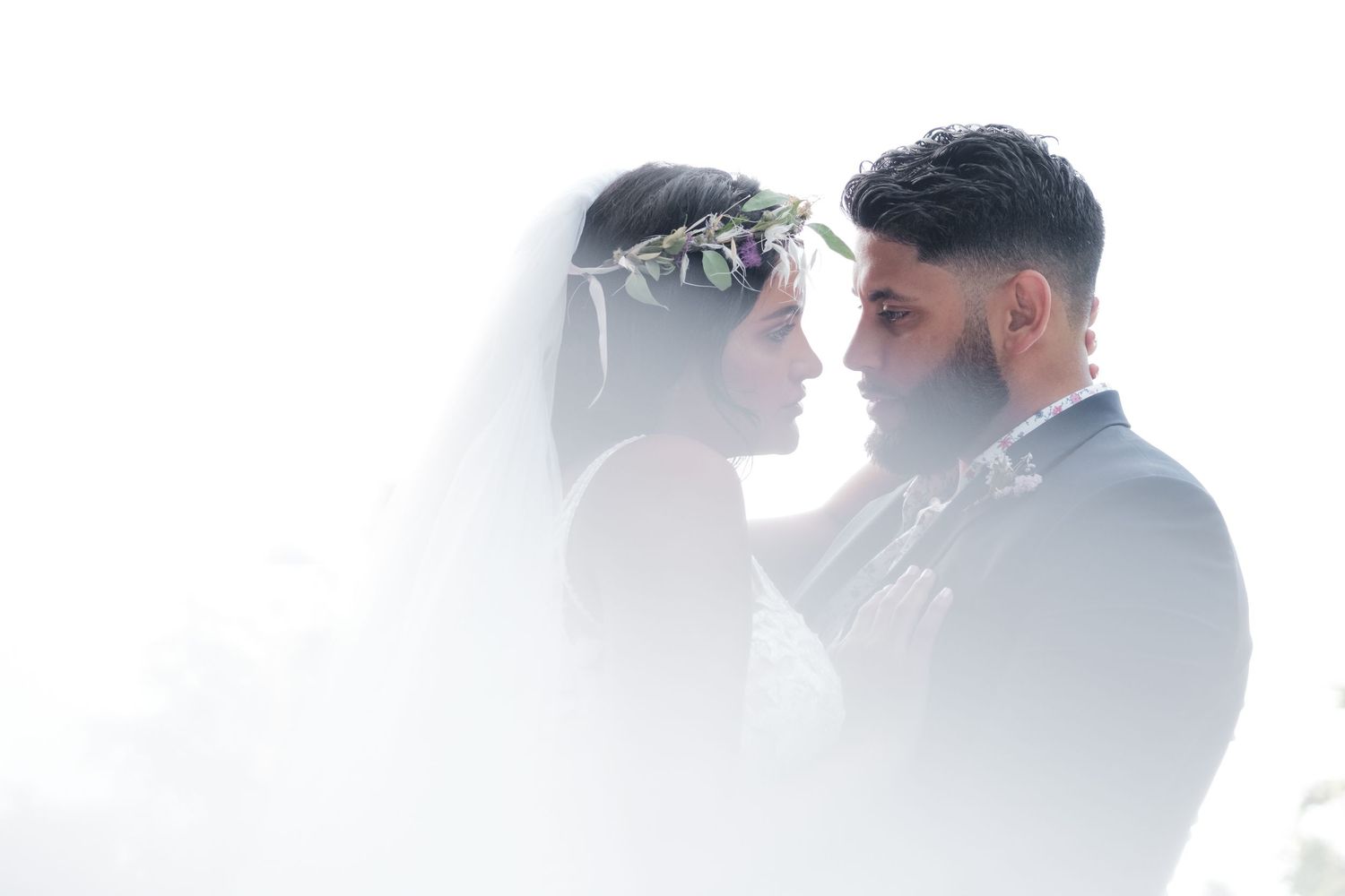 Bride and groom in soft white mist, bride wearing floral crown and veil facing her groom.