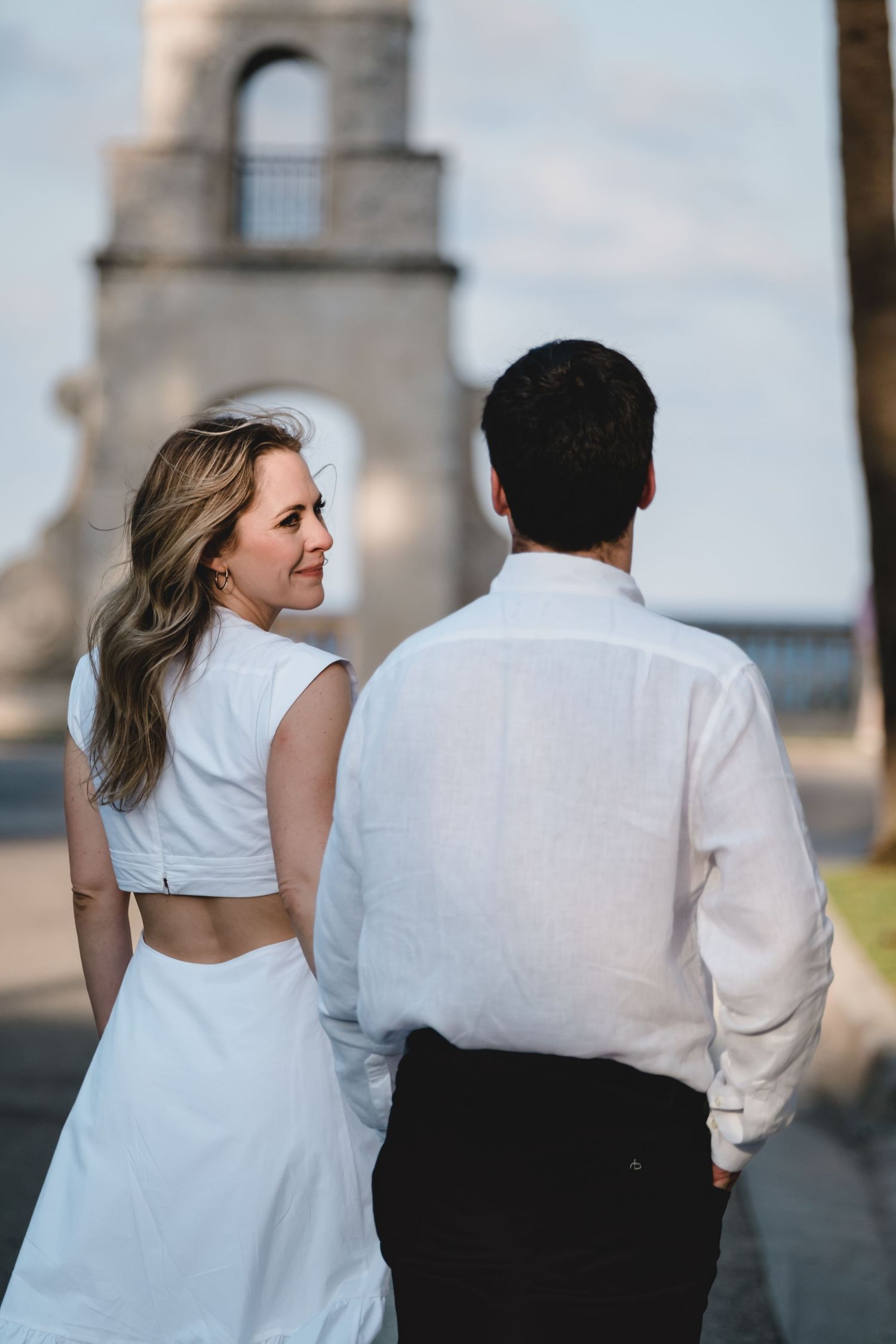 Couple walking hand-in-hand toward historic bell tower at twilight.