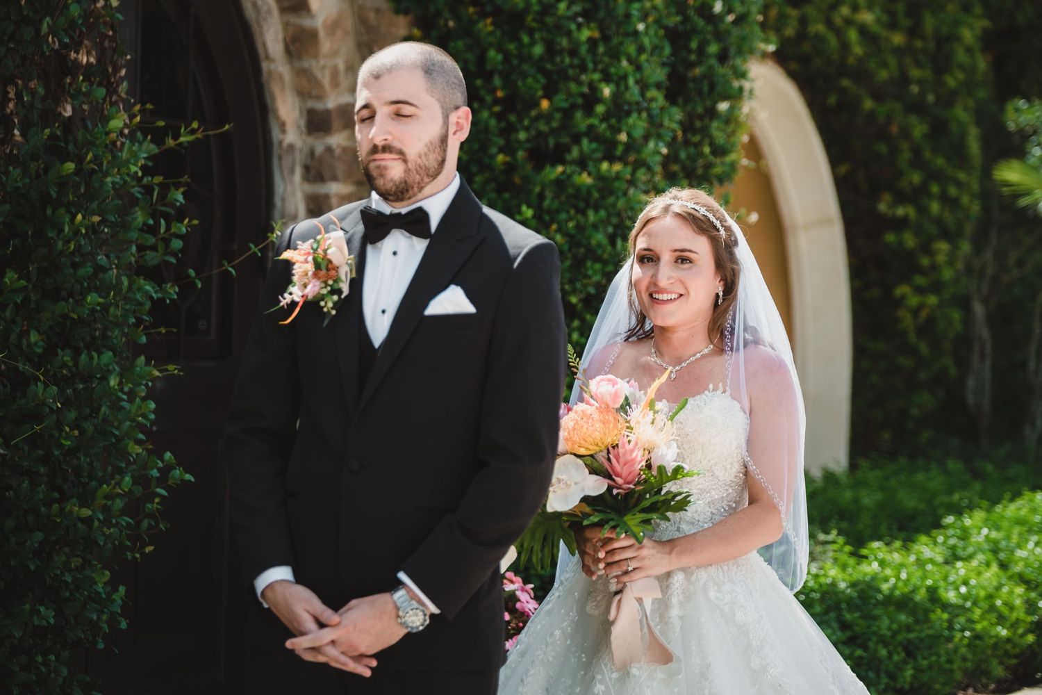 Bride and groom share a first look moment outdoors, bride holding colorful bouquet in lace wedding gown.