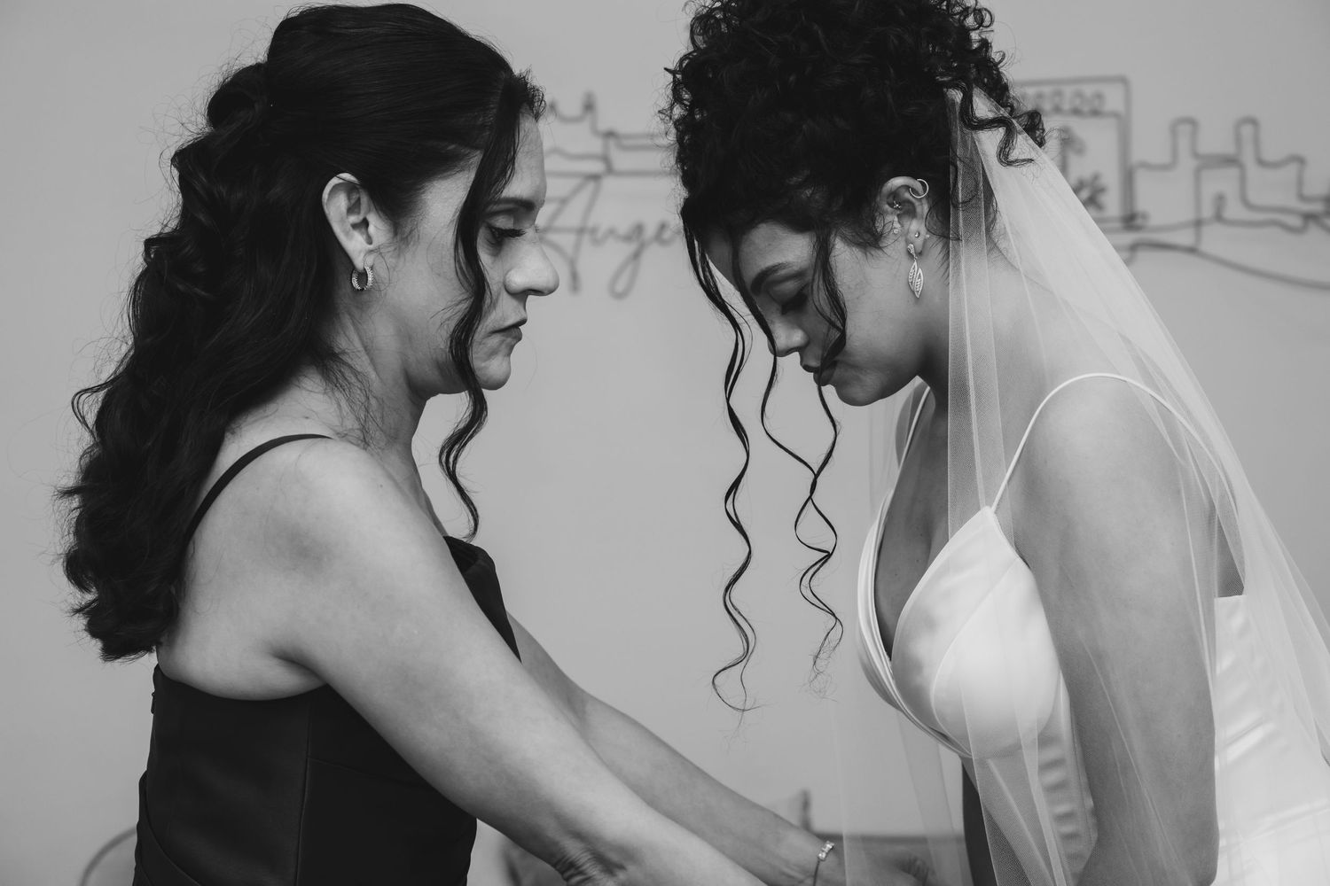 Black and white photo of a bride in white gown and veil being helped by a woman in a dark dress.