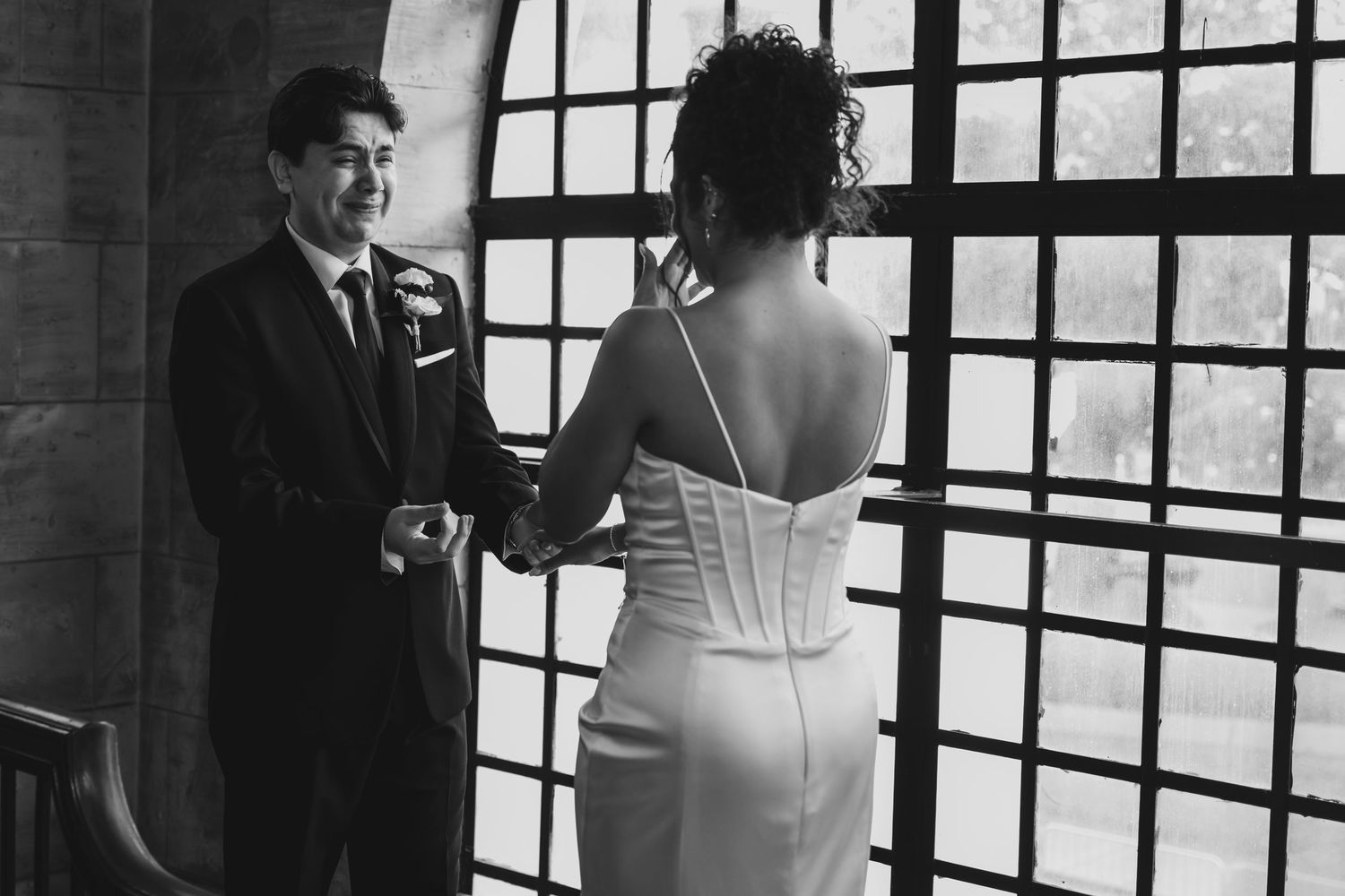 Black and white photo of a groom smiling at his bride during a first look moment inside an elegant venue.