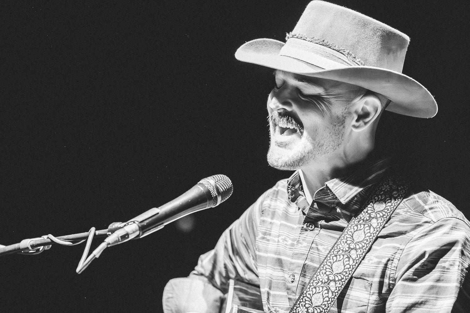 Schwarz-Weiß-Foto eines singenden Country-Musikers, der auf der Bühne mit Cowboyhut bei einem Live-Konzert auftritt.