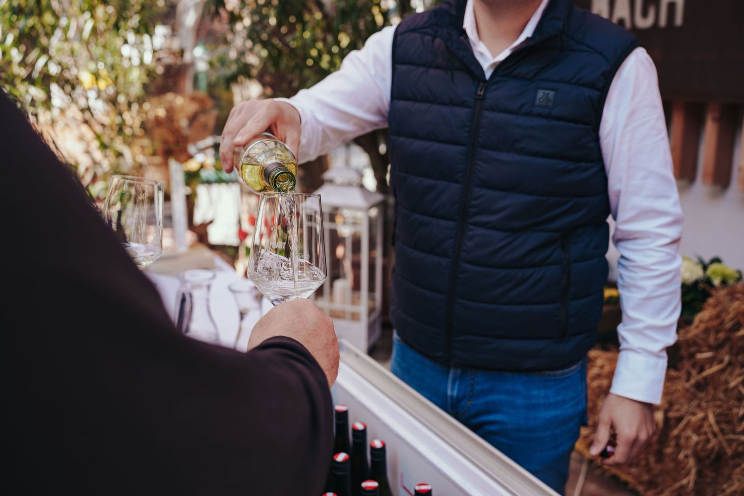 Ein Winzer gießt bei einer Outdoor-Weinveranstaltung Weißwein in Gläser für einen Gast.