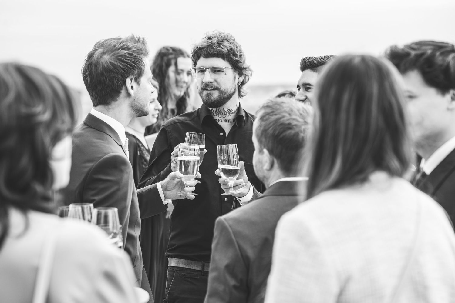 Schwarz-Weiß-Foto von Hochzeitsgästen, die sich bei einem eleganten Empfang mit Champagnergläsern unterhalten.