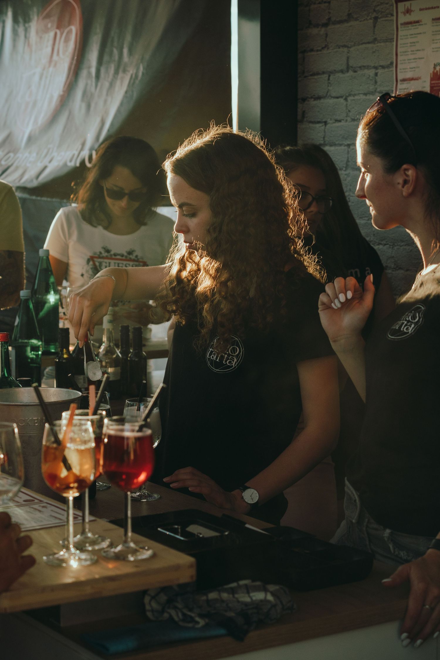 Eine lockiger Barkeeperin schenkt Getränke an einer Bar ein, auf der bunte Cocktails auf der Theke stehen.