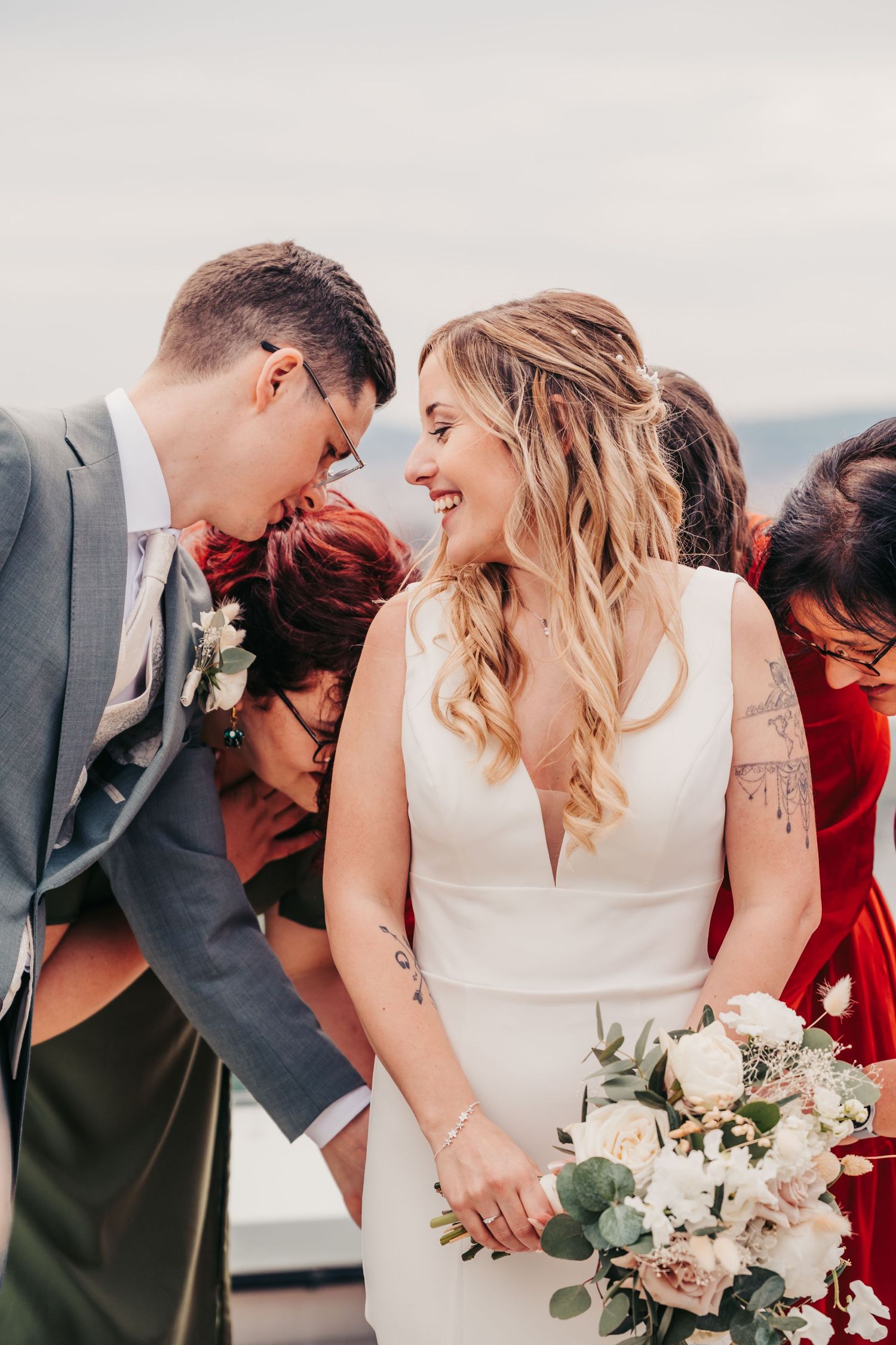 Braut und Bräutigam berühren sich intim mit der Stirn, umgeben von Gästen bei einer Dachterrassen-Hochzeit.